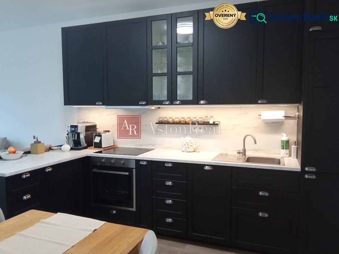 VÝMENA! Nový 2+kk s park. miestom a lodžiou za 3+1, Rača, Bratislava - Kuchyňa v 2-izbovom byte s tmavými skrinkami a dreveným dekorom stola.