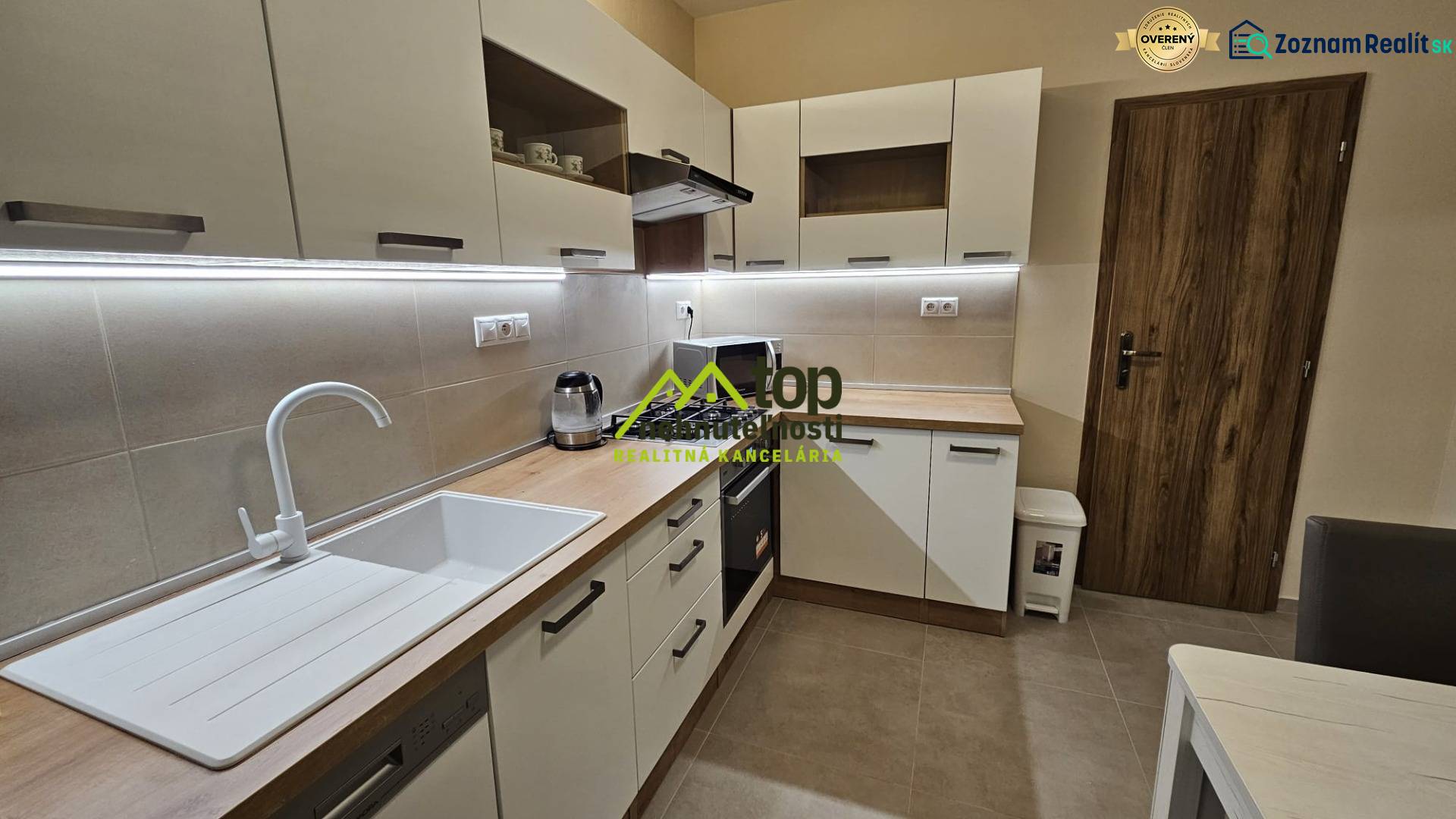 Prenájom 2 izbový byt v Topoľčanoch, sídlisko JUH - Kuchyňa v 2-izbovom byte s bielymi skrinkami a podlahou s dreveným dekorom.