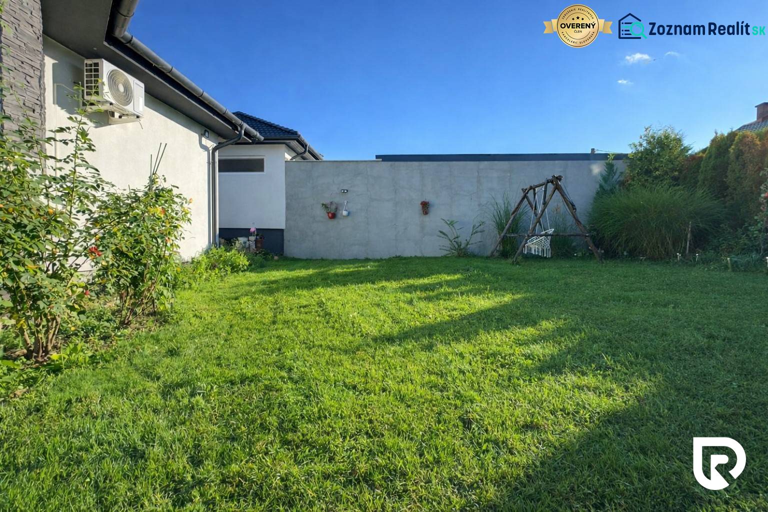 RADO I 4-IZBOVY murovaný ROD.DOM I RAJKA - Záhrada rodinného domu v Rajke s trávnikom, hojdačkou a kríkmi popri stene.