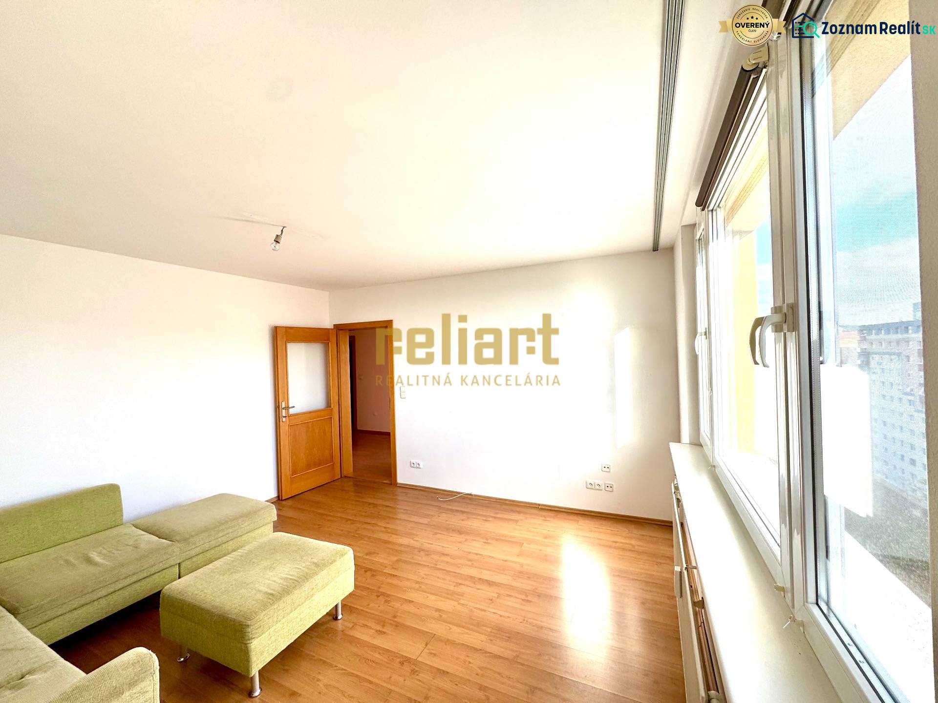 Zrekonštruovaný 3i byt na začiatku Petržalky, električka, les, výhľady - Obývacia izba s podlahou s dreveným dekorom, zelenou sedačkou a veľkými oknami v 3-izbovom byte.