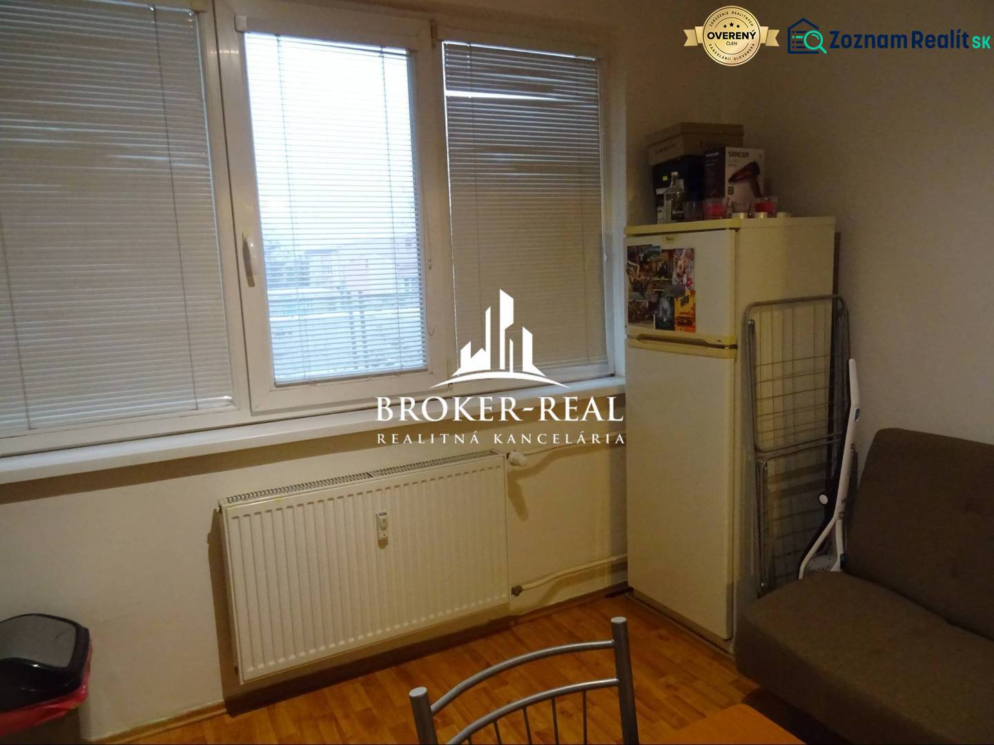 1 - izbový byt Košice, Popradská - Izba s oknom, prúžkovanými žalúziami, podlahou s dreveným dekorom a chladničkou v 1-izbovom byte.