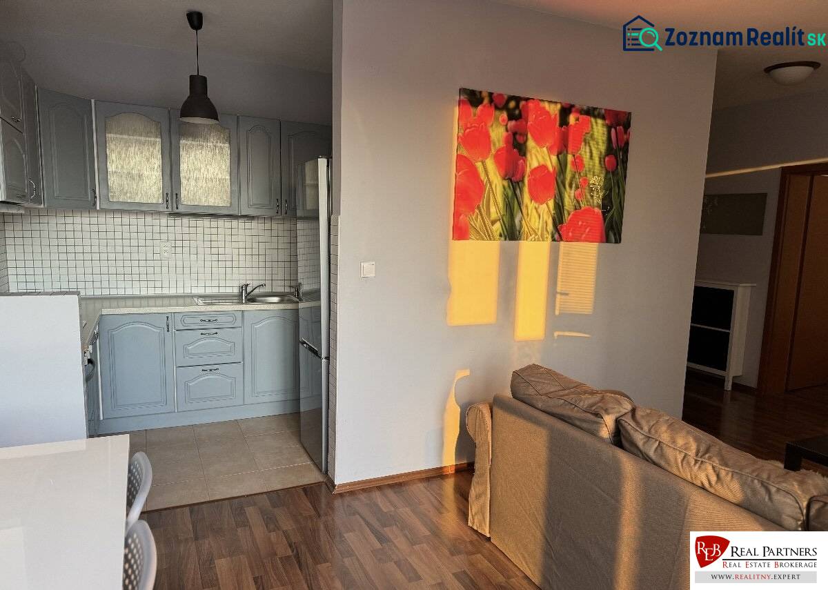Prenájom 2-izb byt v uzavretom areáli Bratislava II - Kuchyňa s modrou linkou, stolom, pohovkou a podlahou s dreveným dekorom v 2-izbovom byte.