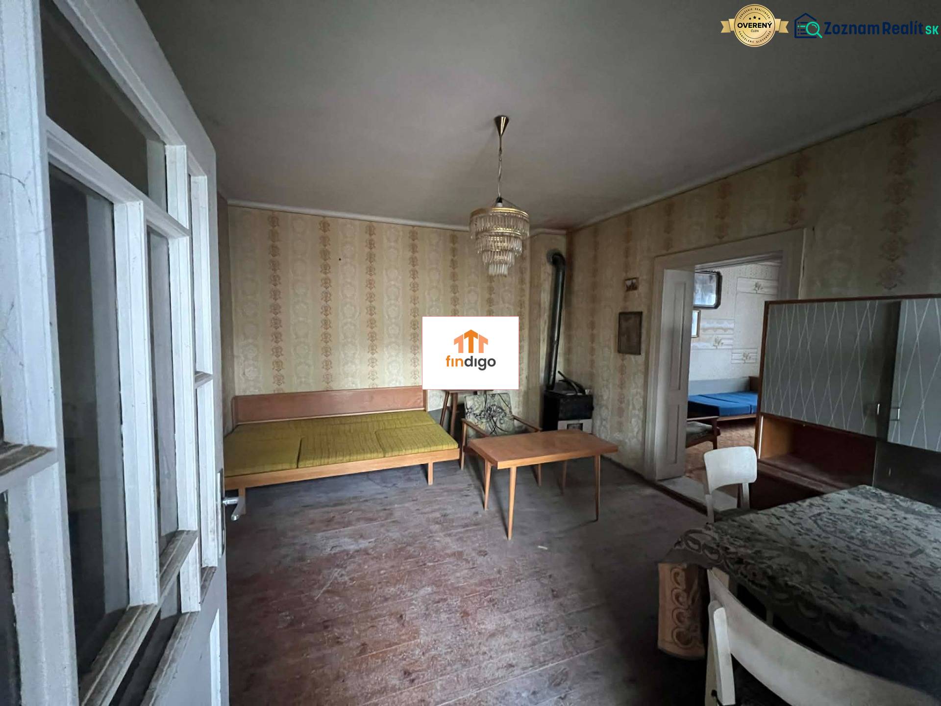 PREDAJ - Rodinný dom na rekonštrukciu s veľkým pozemkom – Kuraľany - Izba v rodinnom dome s retro nábytkom, tapetami a podlahou s dreveným dekorom.