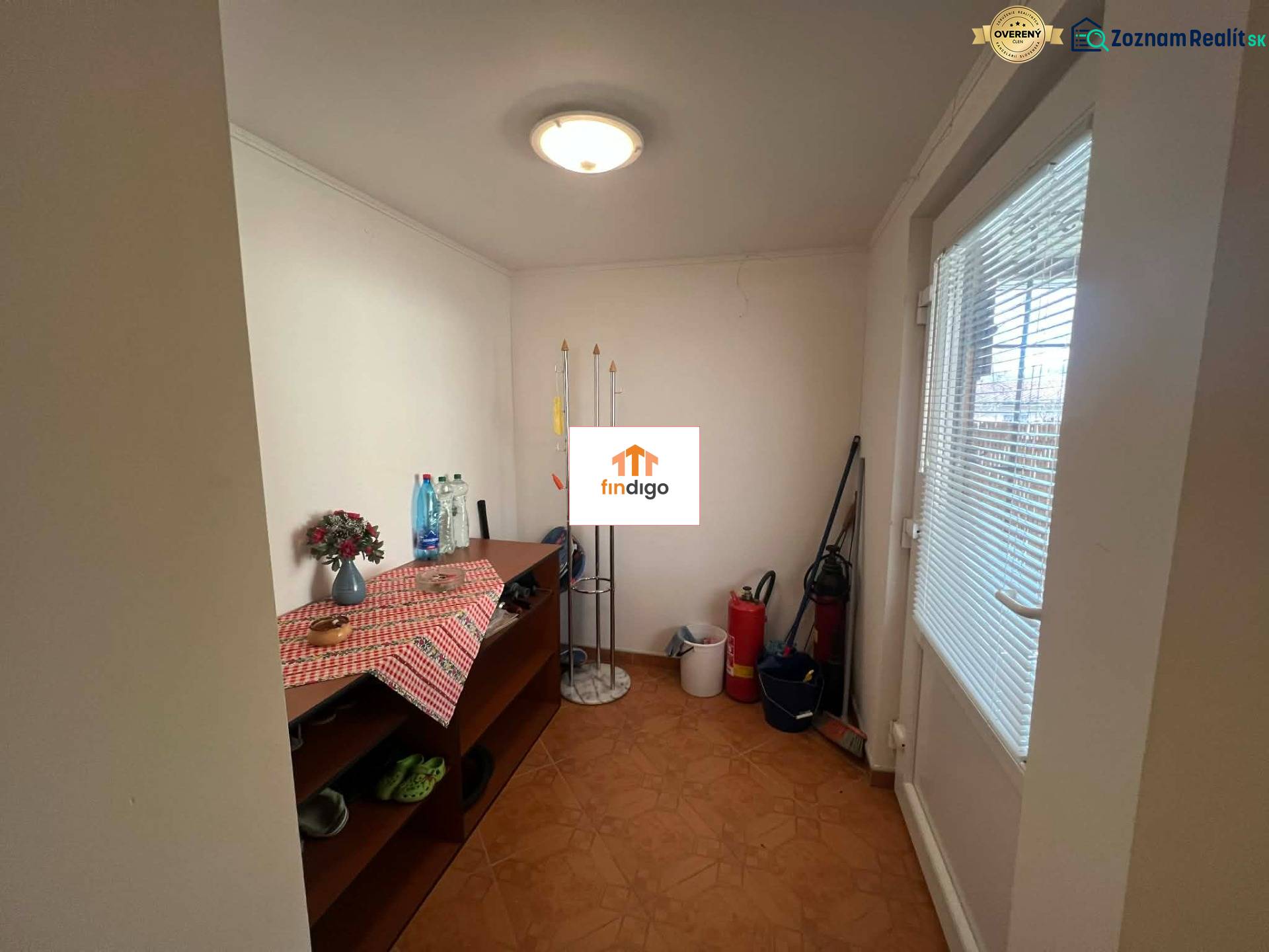 PREDAJ - Zrekonštruovaná rekreačná chata - Chľaba - Interiér chaty s komodou, čistiacimi potrebami a kvetinou na stole.