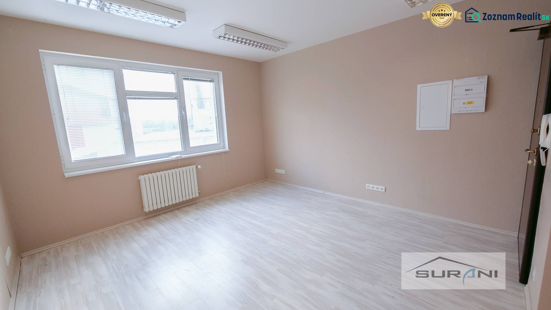  	 Bez Provízie | Kancelária 17m2 | Paulínyho ulica | Bratislava - Kancelária s veľkým oknom, podlahou s dreveným dekorom a radiátorom.