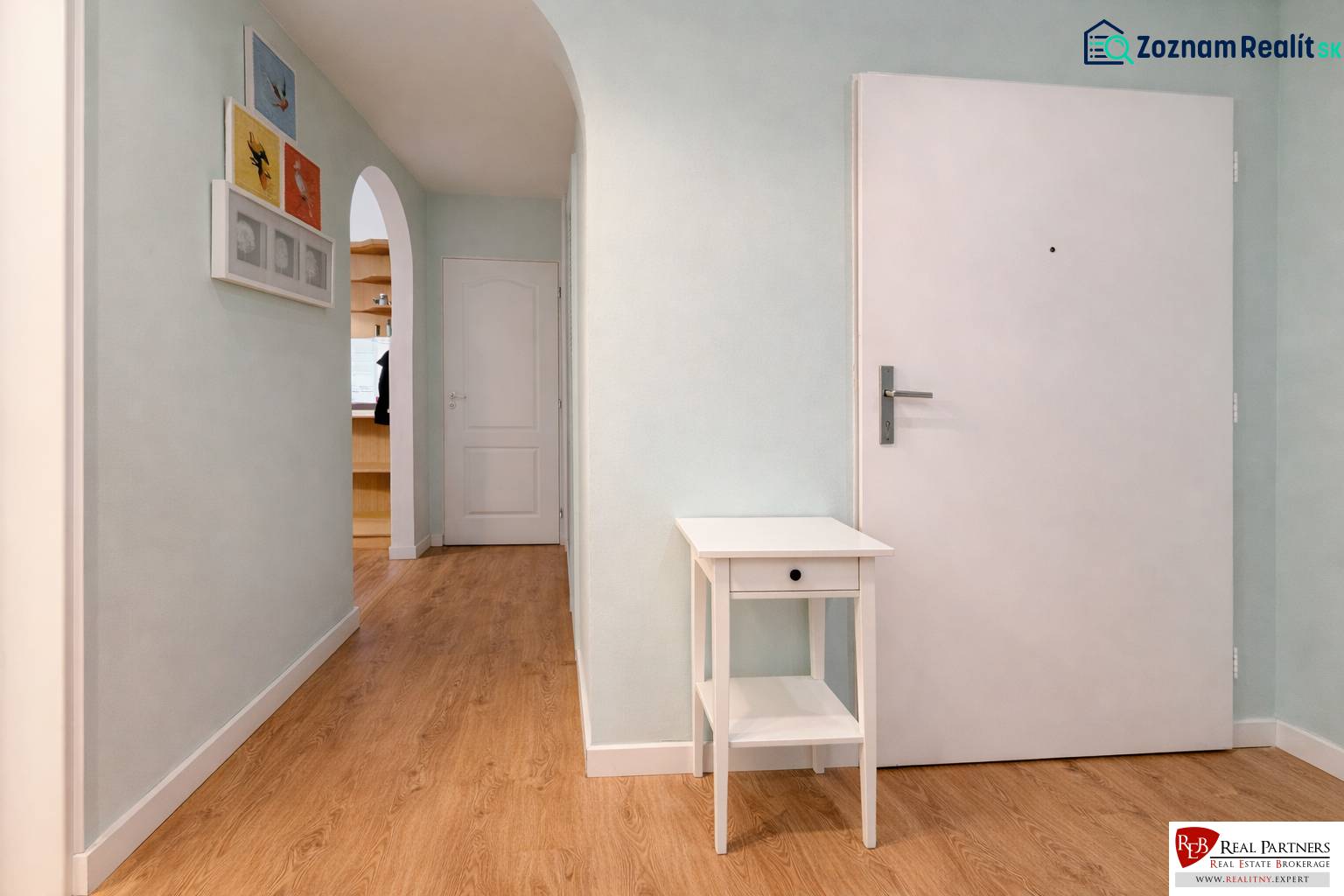 Predaj 4+1 izbový byt, 110 m2, 2 balkóny, Obchodná ul, centrum BA - Chodba v 4-izbovom byte so stolíkom a dekoráciami na stenách, podlaha s dreveným dekorom.