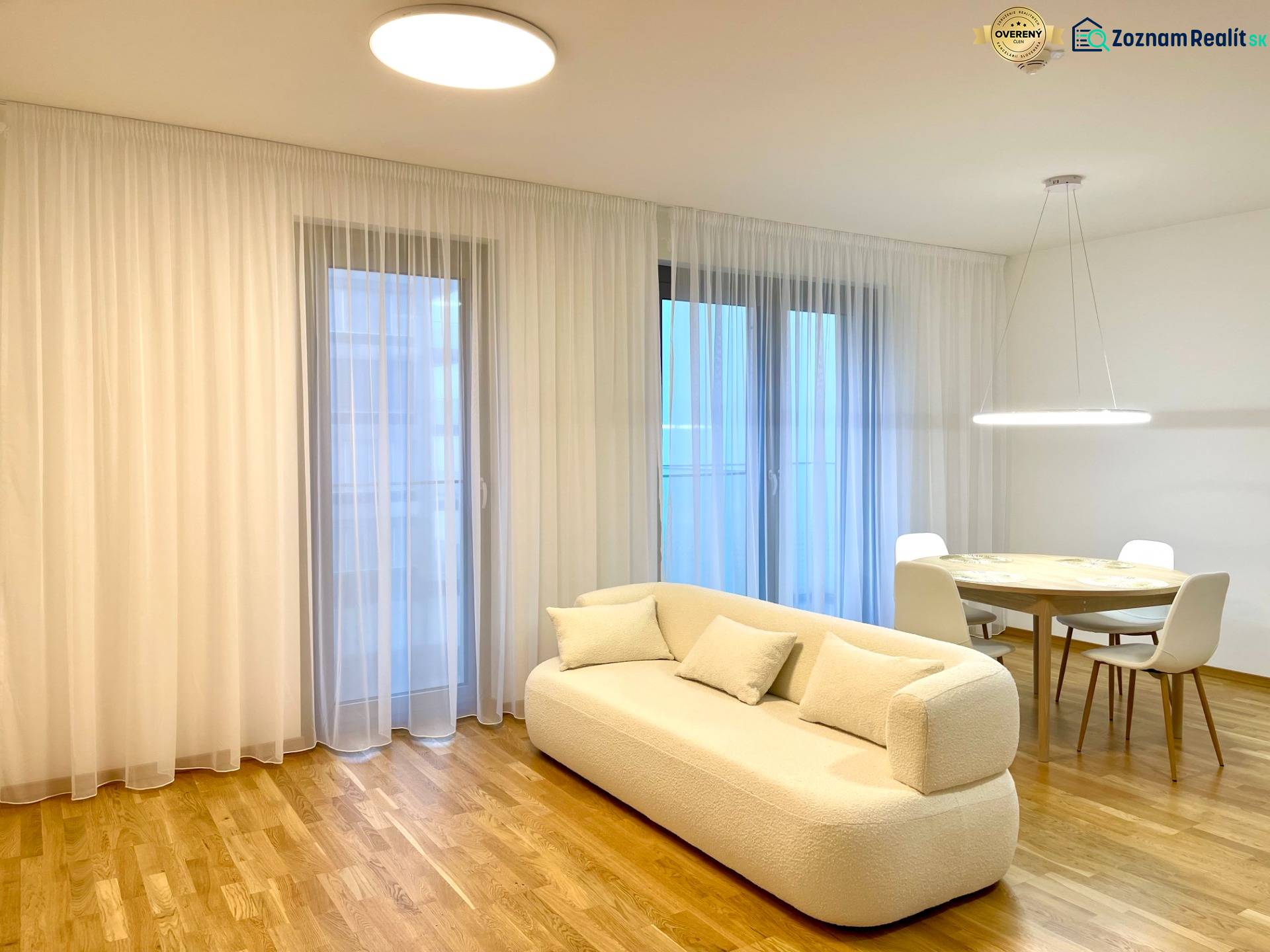 I 3 i byt s parkovaním v rezidenčnom komplexe METROPOLIS - Svetlá obývacia izba v 3-izbovom byte s bielou sedačkou a podlahou s dreveným dekorom.