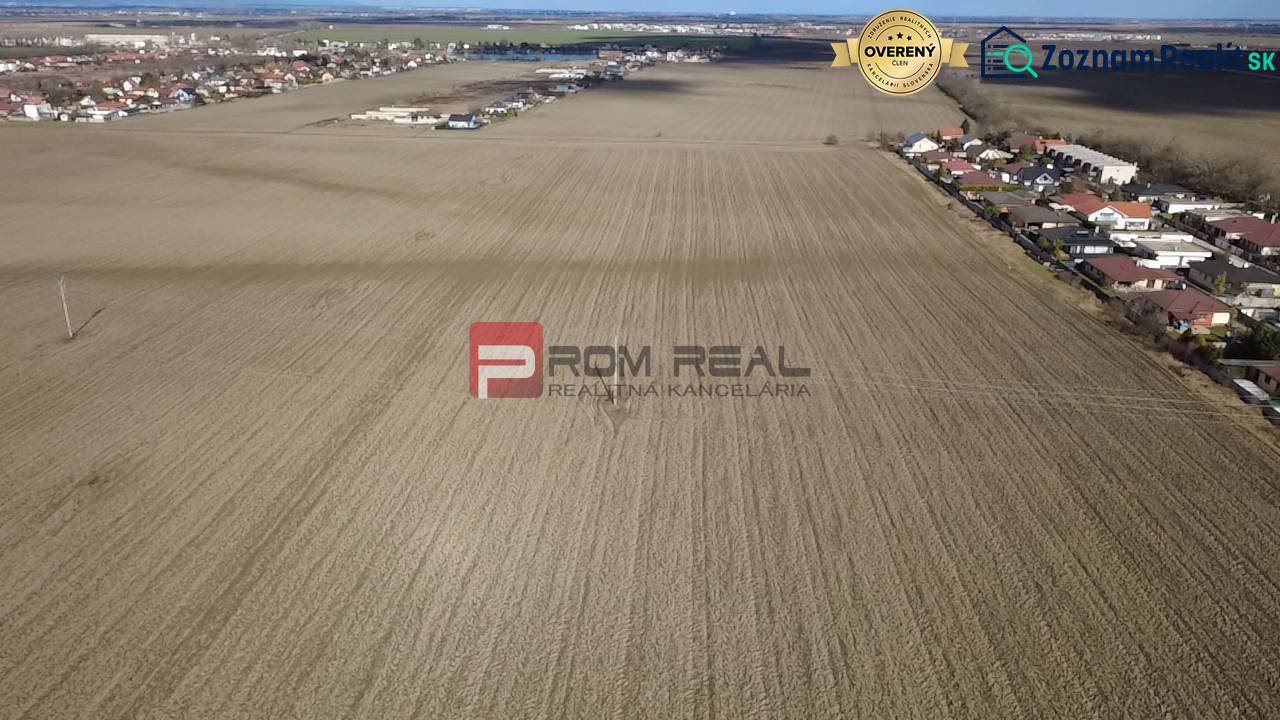 INVESTIČNÁ PRÍLEŽITOSŤ – Pozemok v obci Dunajská Lužná - Rozľahlé poľnohospodárske a lesné pozemky v okolí Dunajskej Lužnej, s viditeľnou obytnou zástavbou.