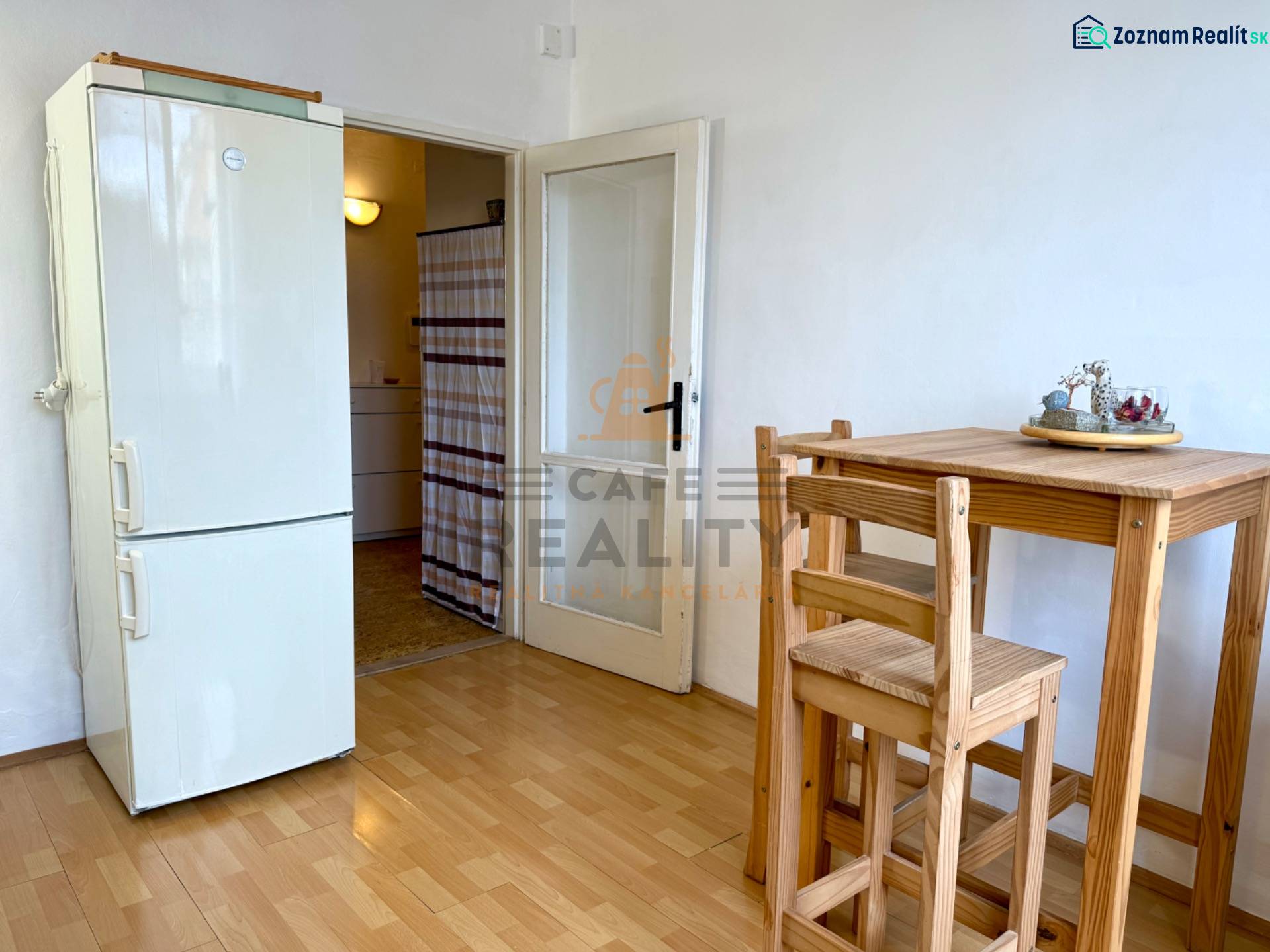 PRENÁJOM 1 izbový byt, 40 M2, Bratislava, Ružinov, Košická ulica, NIVY - Kuchyňa v 1-izbovom byte s dreveným stolom, stoličkami a chladničkou, podlaha s dreveným dekorom.
