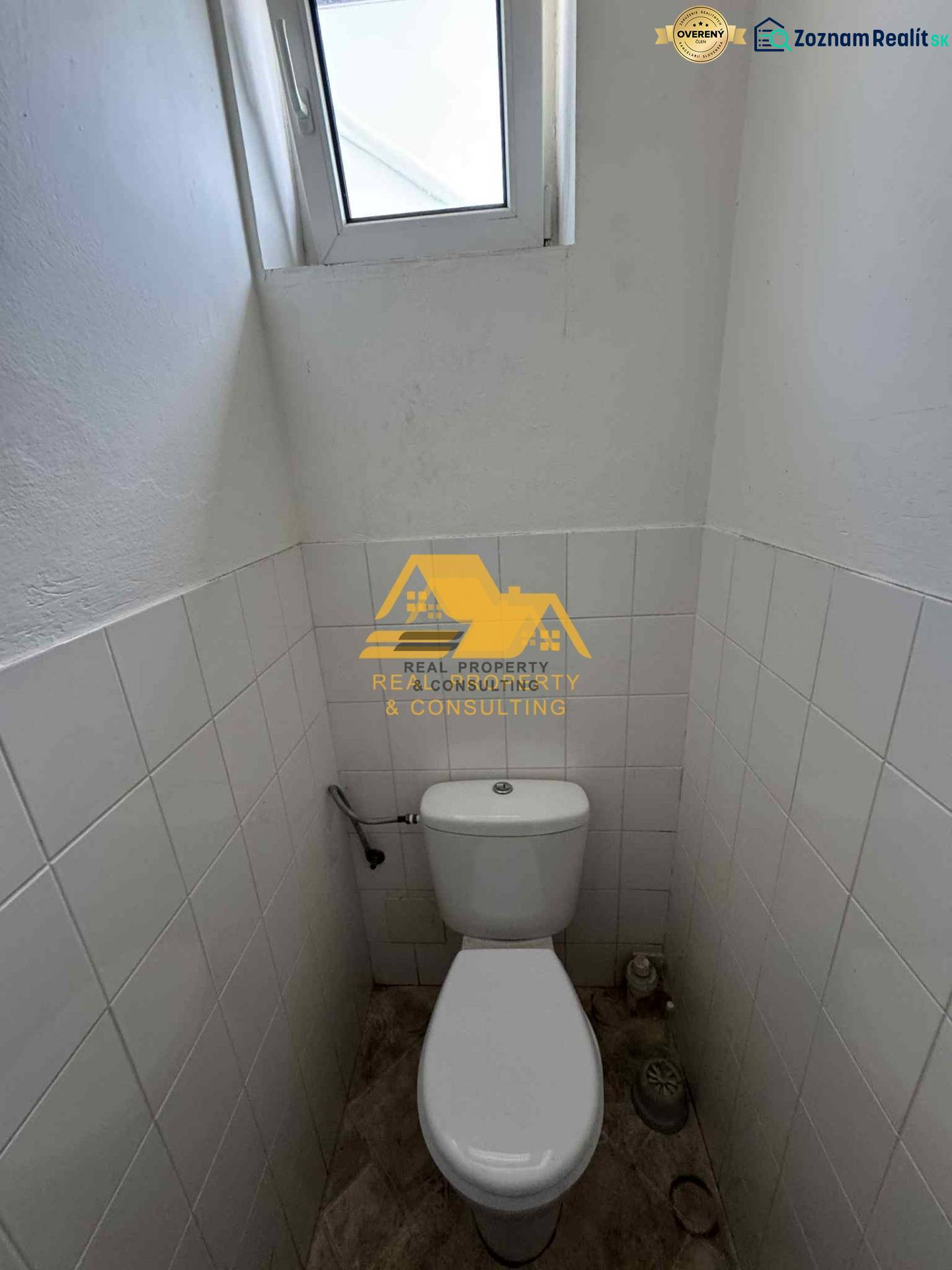 Prenajmem garsónku v Nesvadoch - Kompaktná toaleta s oknom, biele dlaždice, podlaha s dreveným dekorom.