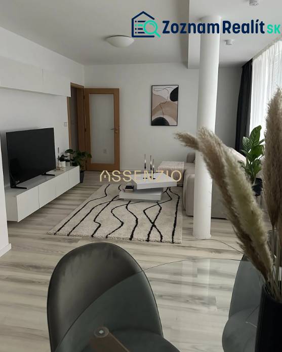 - PRENÁJOM - 2 IZBOVÝ BYT - DOLNÁ UL. - STARÉ MESTO - Obývačka 2-izbového bytu s podlahou s dreveným dekorom, bielym nábytkom a kobercom.