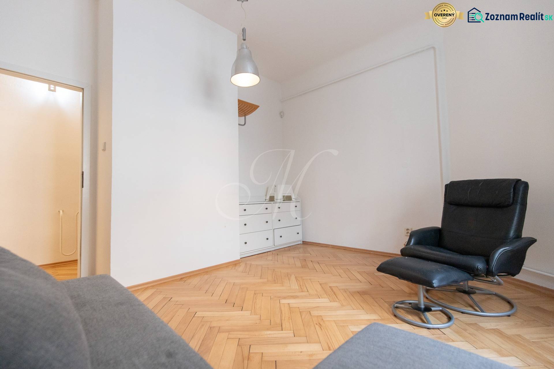 Priestranný 4-izbový byt s predzáhradkou, Staré Mesto - Interiér 4-izbového bytu s kreslom, bielou komodou a podlahou s dreveným dekorom.