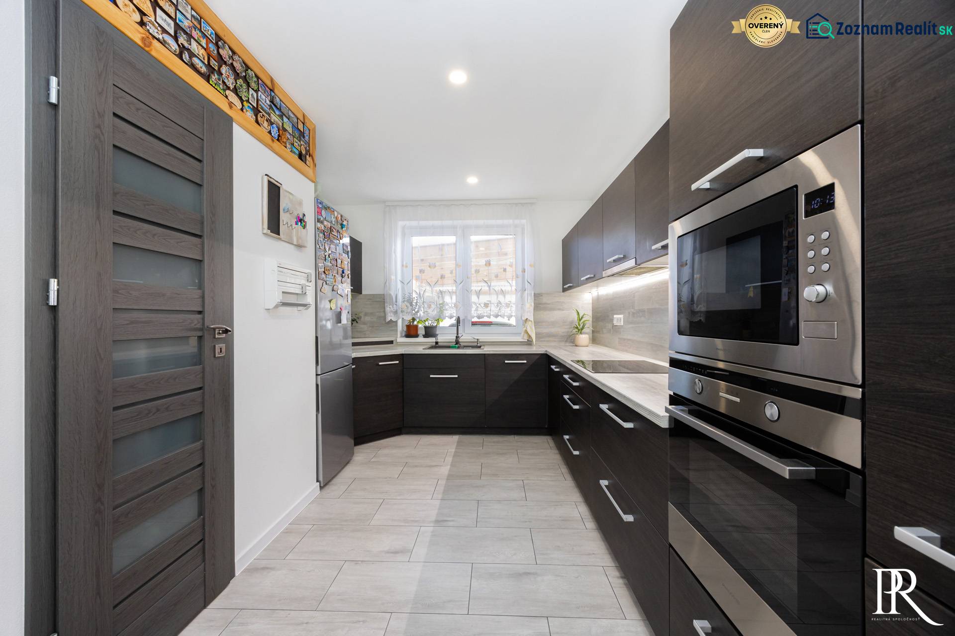 NOVOSTAVBA BUNGALOVU S MNOŽSTVOM PRIESTORU, v slepej ulici, Pružina - Kuchyňa v rodinnom dome s tmavým nábytkom a dlažbou dekoru dreva.