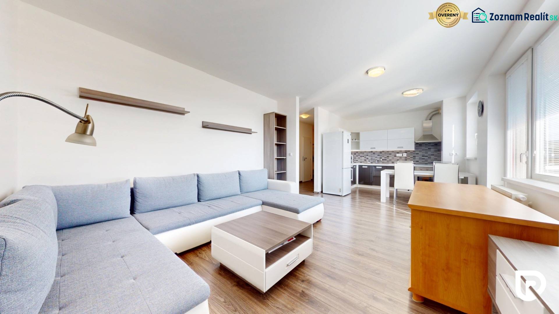 | Priestranný 2,5-izb. byt s walk-in šatníkom | parkovanie | - Obývacia izba s kuchyňou v 2-izbovom byte, dominujú neutrálne tóny a podlaha s dreveným dekorom.