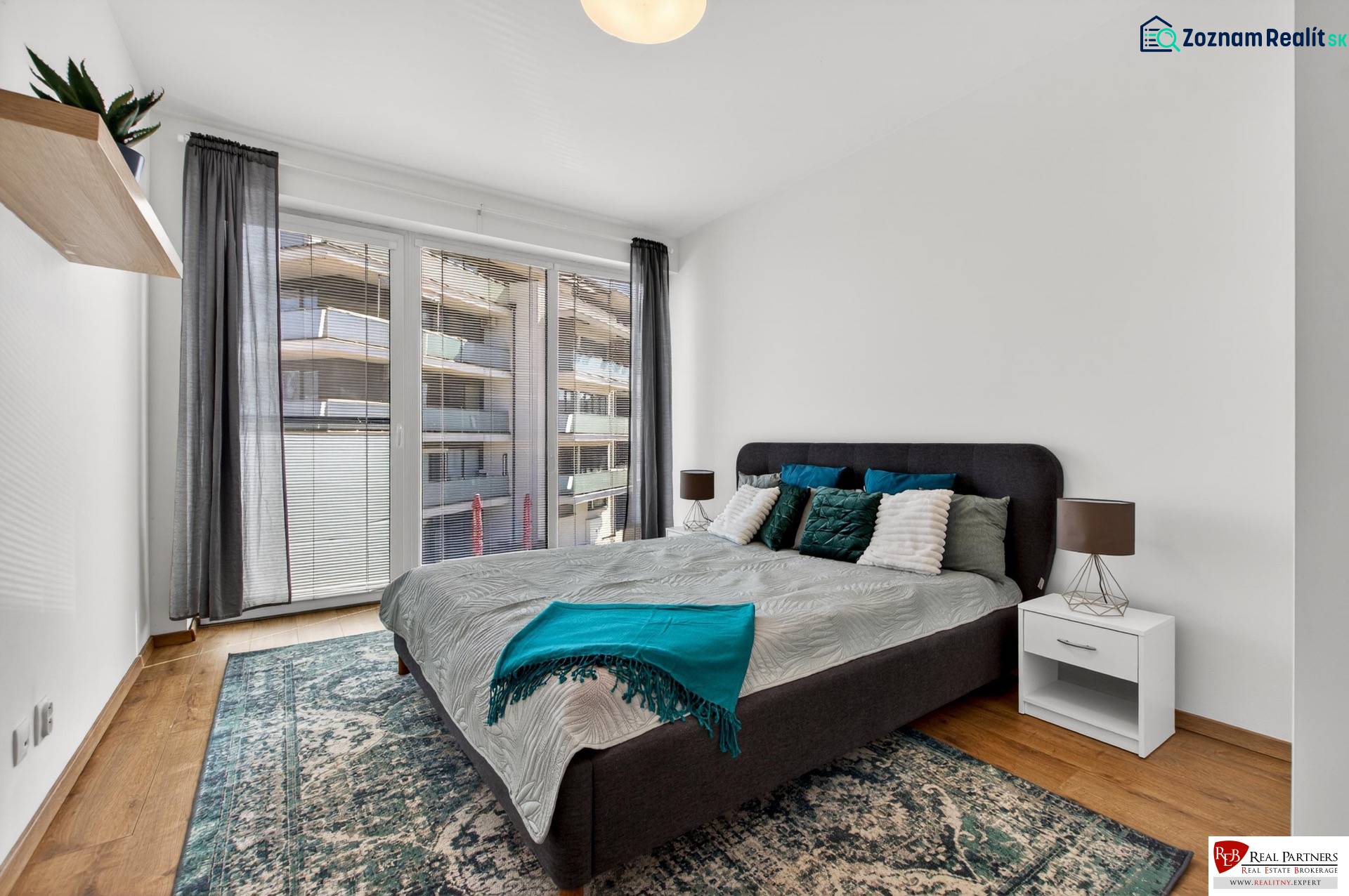 Predaj 2-izbový byt GREEN VILLAGE, 51m2, loggia, Dunajská Lužná - Spálňa s veľkou posteľou, balkónovými dverami a podlahou s dreveným dekorom v 2-izbovom byte.