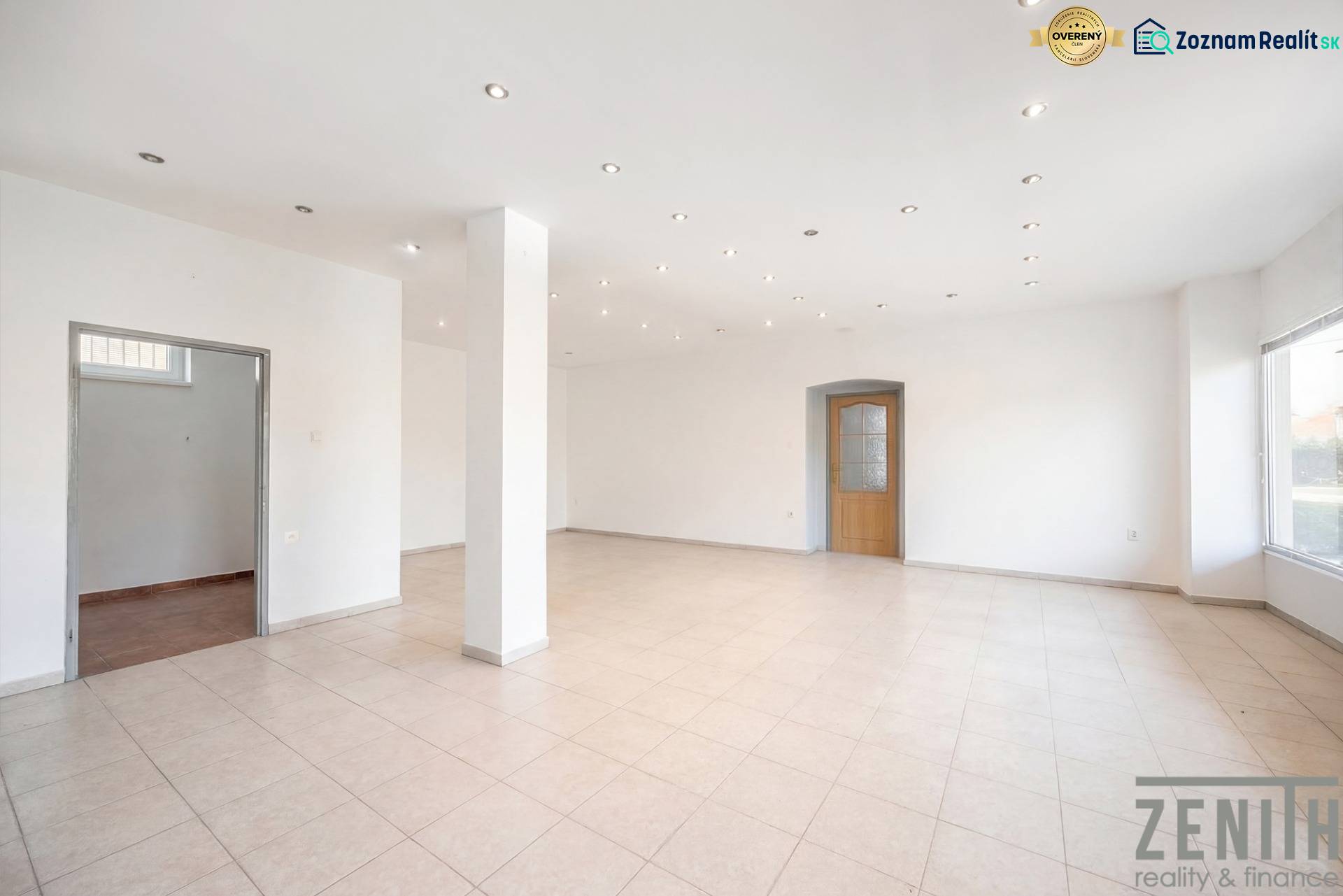 Komerčný objekt s pozemkom – možnosť zmeny na rodinný dom - Priestranné obchodné priestory s bielymi stenami, dlažbou a rozsvietenými stropnými svetlami.
