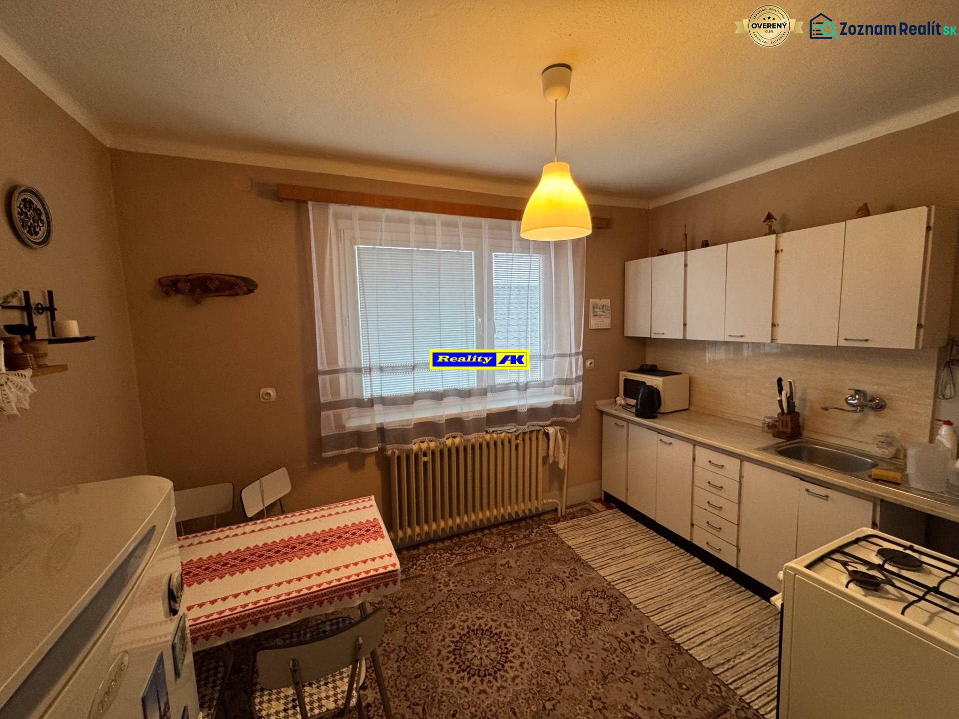 Rodinný dom Martin - Valča - Kuchyňa v rodinnom dome s bielymi skrinkami, vzorovaným kobercom a jedálenským stolom.