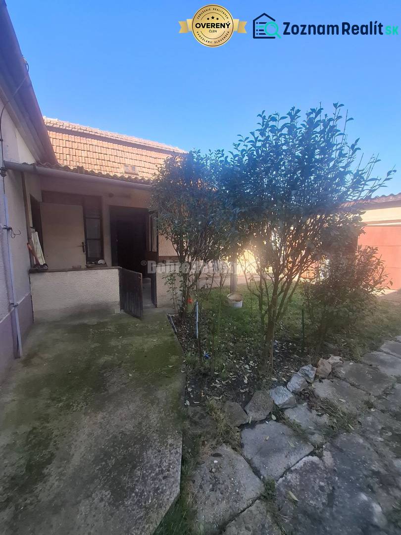 Na predaj rodinny dom v obci Iža. - Rodinný dom v Iži s dvorom, chodníkom a rastlinami pred domom.