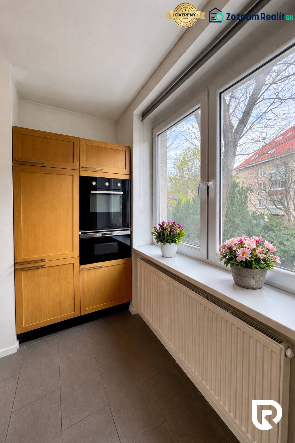 Tichý 2i byt v TOP Lokalite Nív | Trenčianska, BA - Kuchyňa v 2-izbovom byte s dreveným dekorom a veľkými oknami.