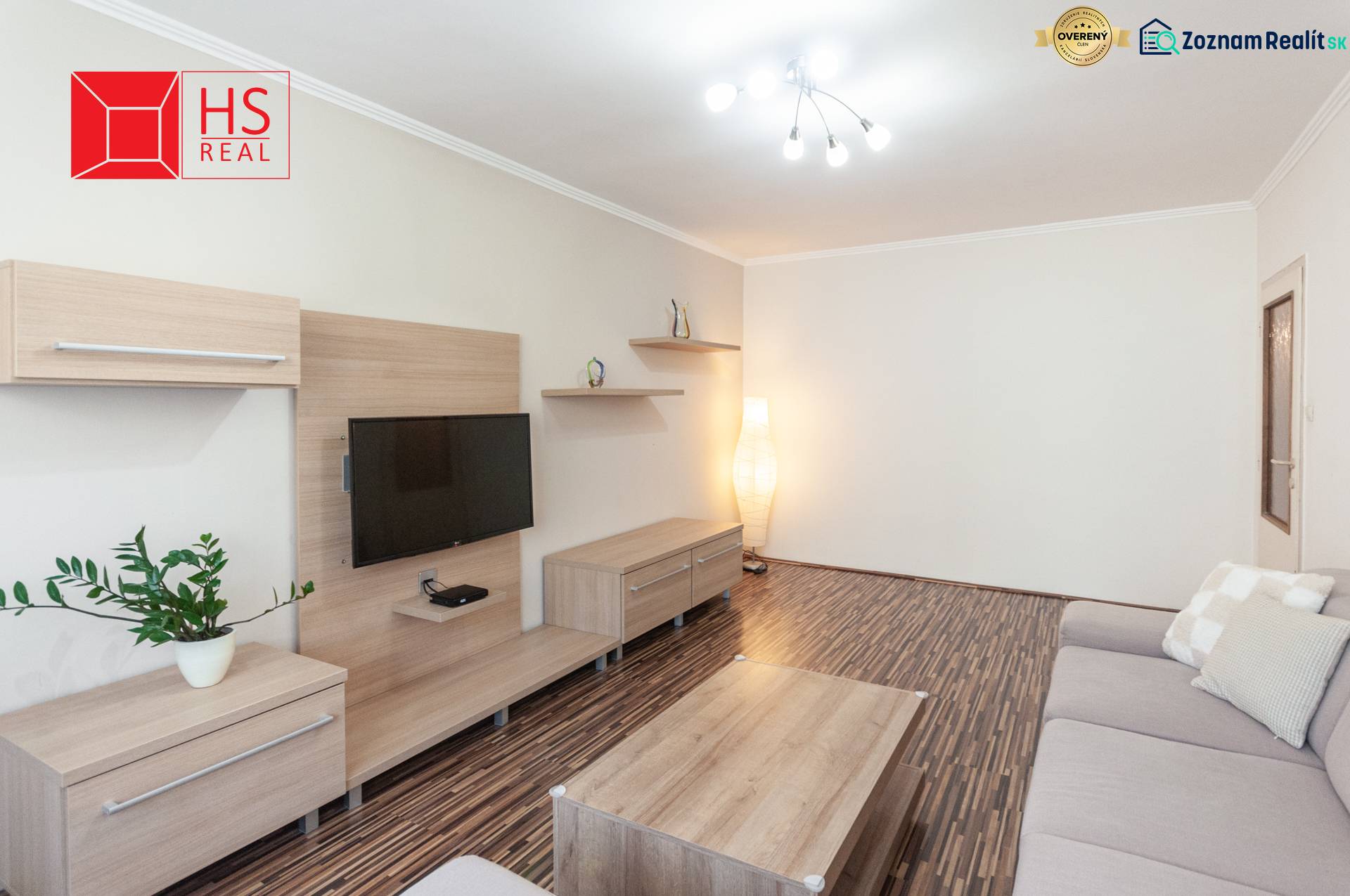 Predaj 3i bytu 84m2 - dva balkóny , Nábrežná v NZ - Obývacia izba 3-izbového bytu s podlahou s dreveným dekorom a sivou pohovkou.