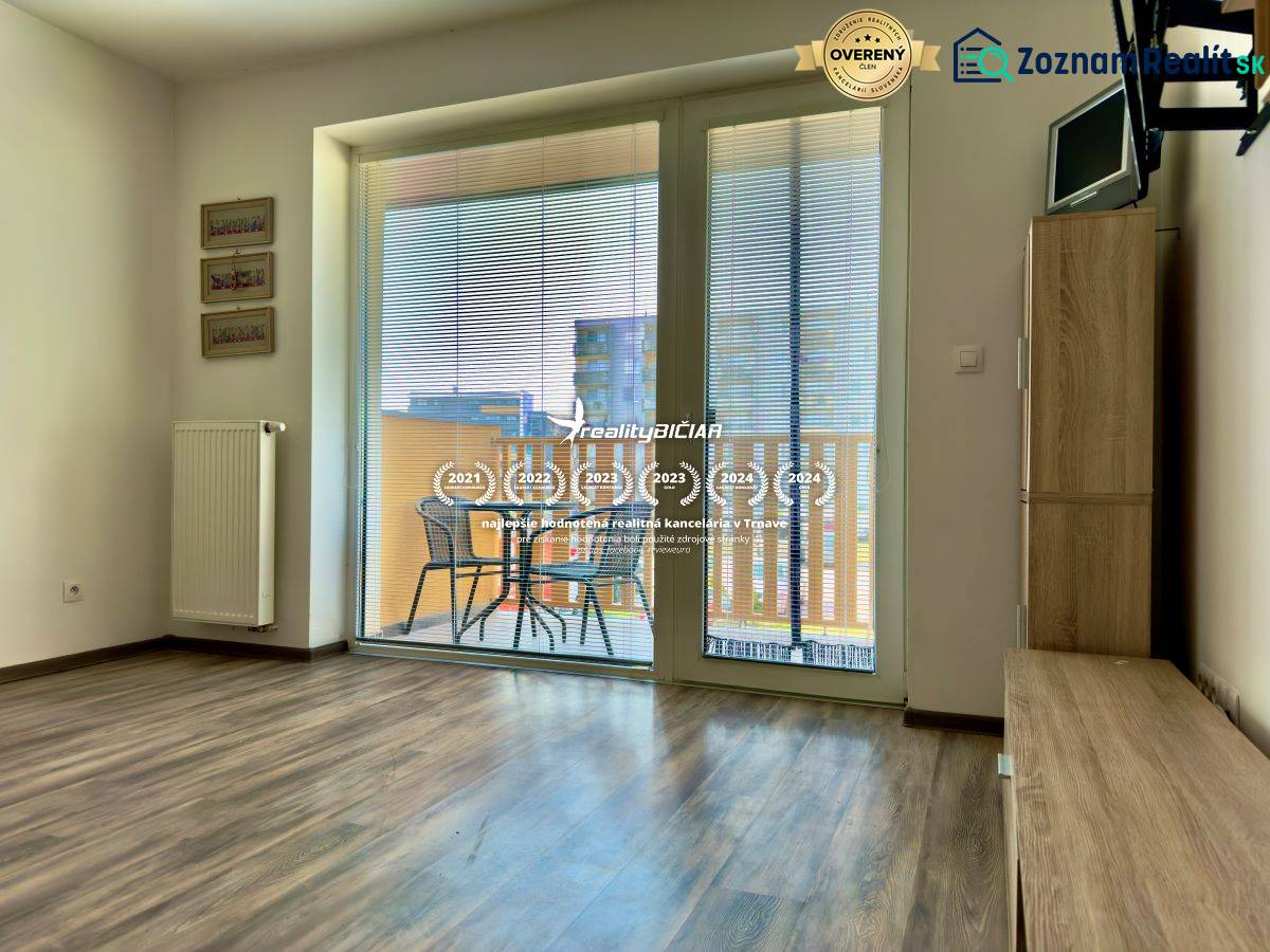 Na predaj moderný 2 izbový byt, komplex MIKO Trnava - Obývacia izba v 2-izbovom byte s podlahou s dreveným dekorom a prístupom na balkón.