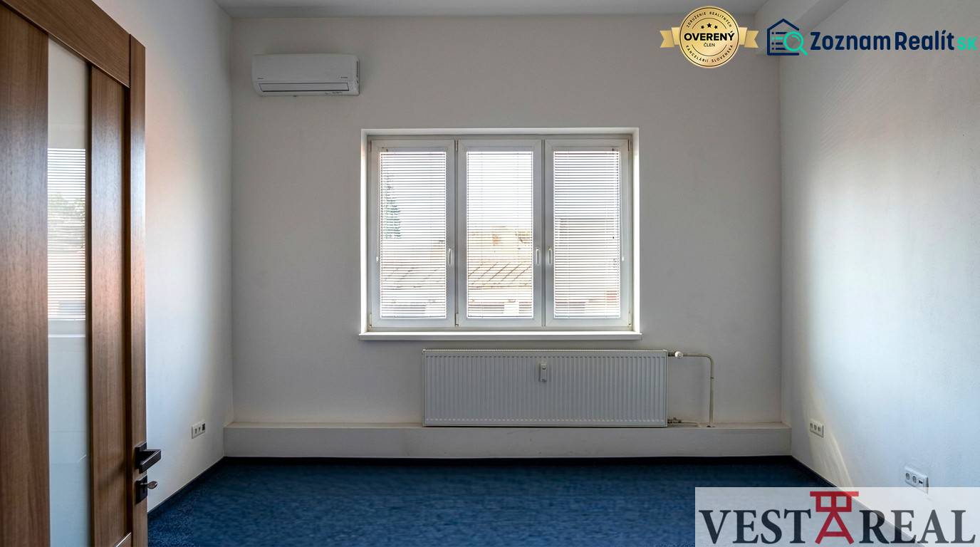 Prenájom klimatizovaná kancelária: 25 m2 a 42 m2 - Trnava Chovateľská - Izba s klimatizáciou a oknom v Kanceláriách, modrý koberec, biele steny.