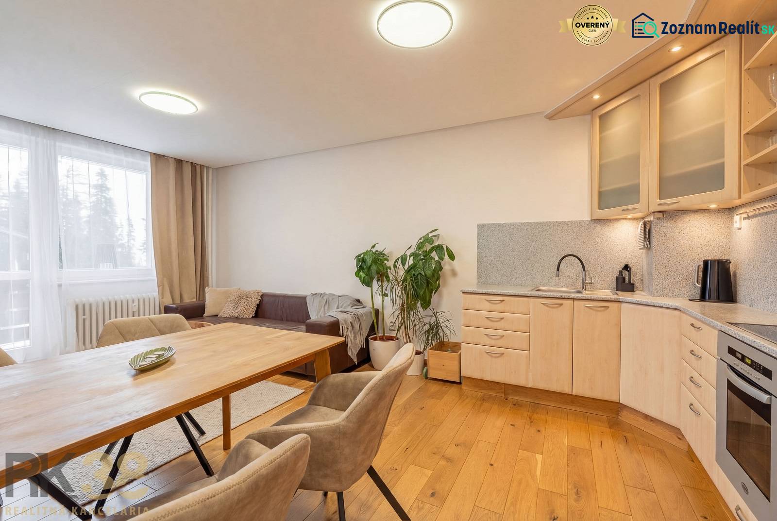 Exkluzívny byt v srdci Vysokých Tatier na Štrbskom Plese - Interiér rekreačného apartmánu s pohovkou, kuchyňou a podlahou s dreveným dekorom.