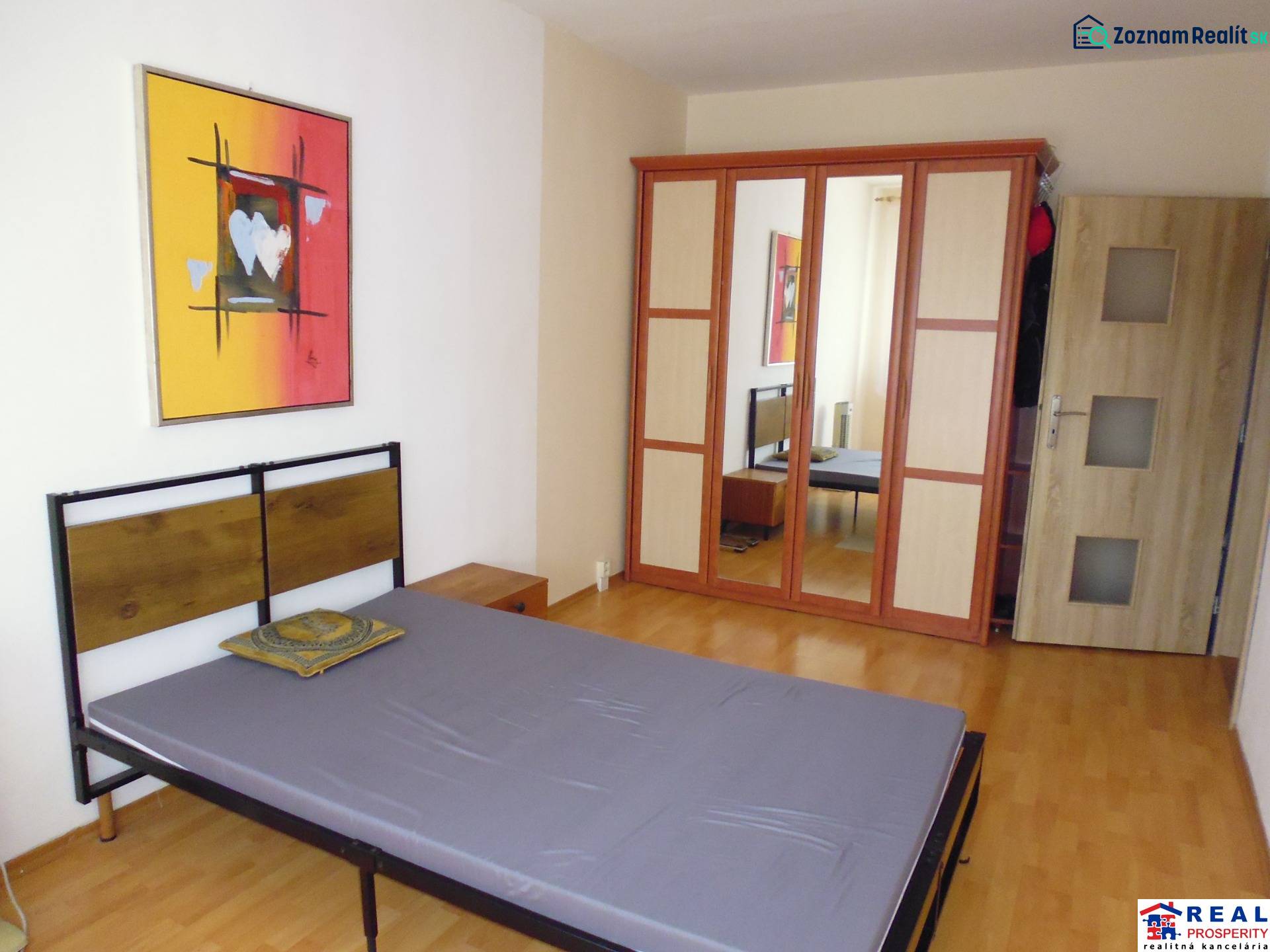 PRENÁJOM: M.NEŠPORA - 2-izbový byt, 58 m2, 7.posch. - Sídlisko III. - Spálňa s posteľou, podlahou s dreveným dekorom a skriňou v 2-izbovom byte.