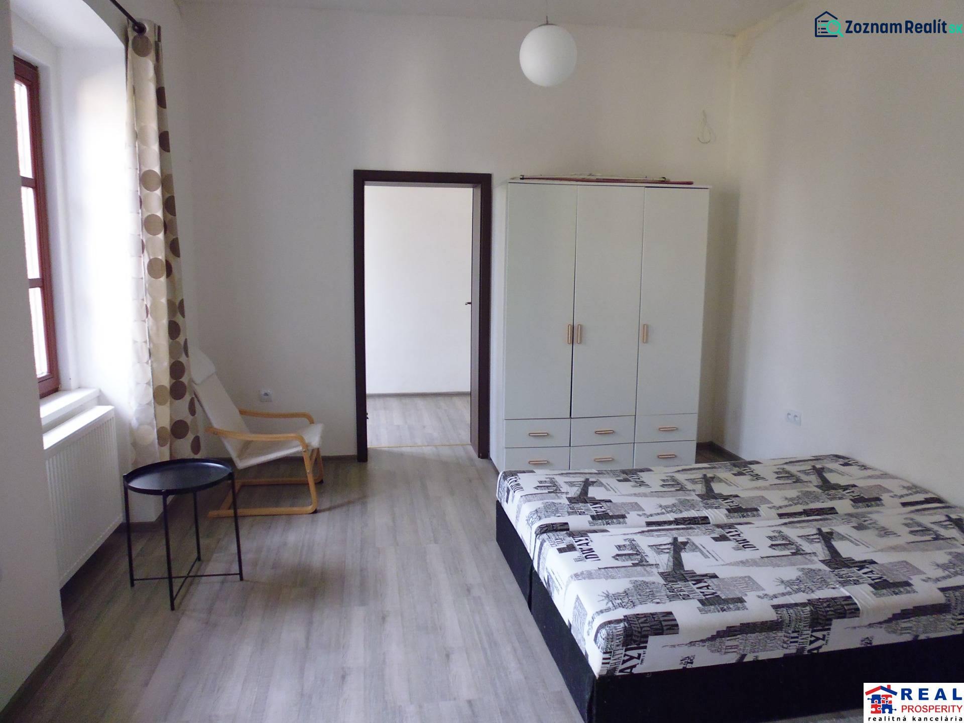 PRENÁJOM: HLAVNÁ - VOĽNÝ 2,5-izbový byt + kuchyňa, kúpeľňa, WC  - Spálňa v 3-izbovom byte s podlahou s dreveným dekorom, skriňou a posteľou.