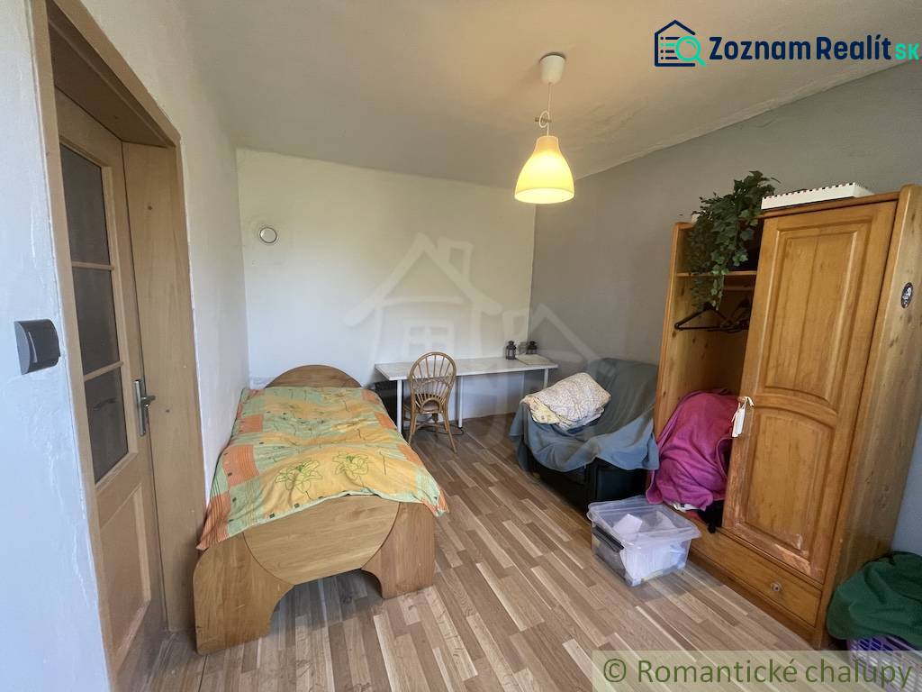 Trojizbový rodinný dom vhodný aj na chalupu v kľudnej časti obce Jatov - Izba v rodinnom dome s posteľou, stolom a podlahou s dreveným dekorom.