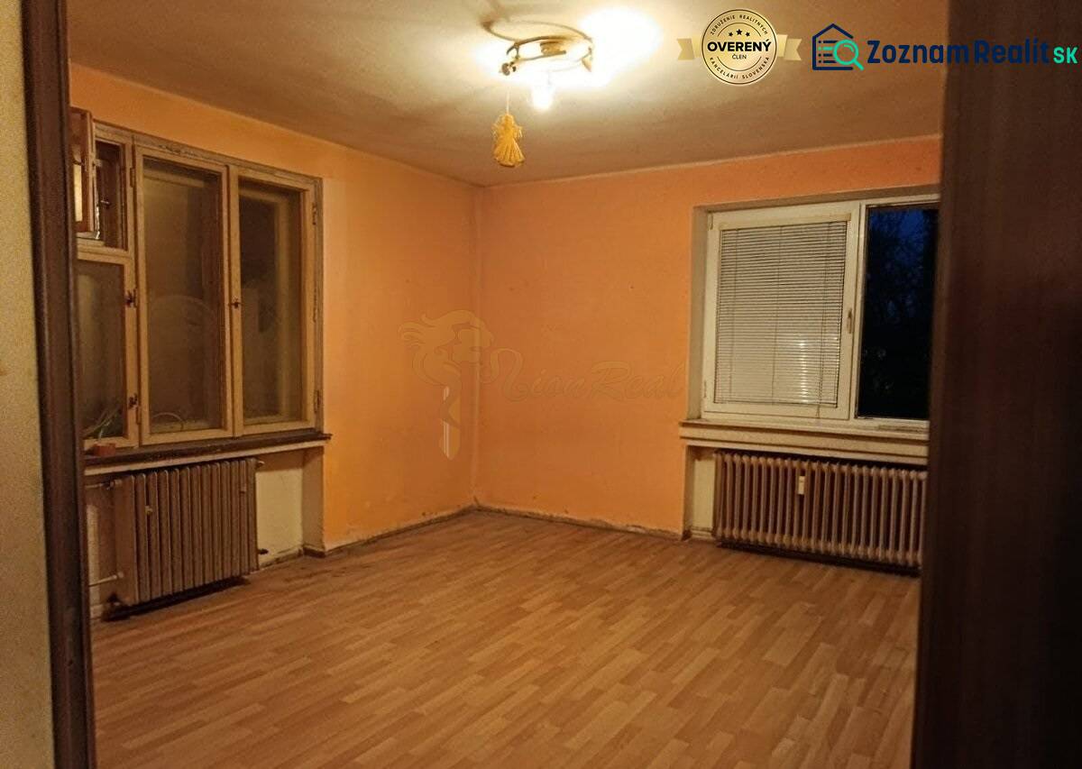 Veľký 2-izb. byt, Olbrachtova ul., Nové Mesto - Izba v 2-izbovom byte, oranžové steny, podlaha s dreveným dekorom, radiátory.