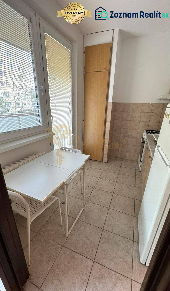 1-izb. byt, J.Stanislava, Karlova Ves, lodžia, 3.p./8 - Svetlá kuchyňa s oknom, jednoduchým stolom a stoličkami v 1-izbovom byte.