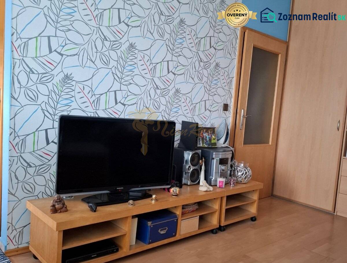 Dvojgarzónka DELUXE, začiatok Petržalky - Obývacia izba v 2-izbovom byte s dreveným dekorom a kvetinovou tapetou.