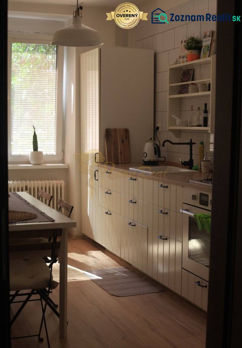 Veľký 2-izb. byt v tehlovom dome, Ružová dolina, Ružinov časť Nivy - Kuchyňa s jedálenským stolom, bielymi skrinkami a podlahou s dreveným dekorom v 2-izbovom byte.