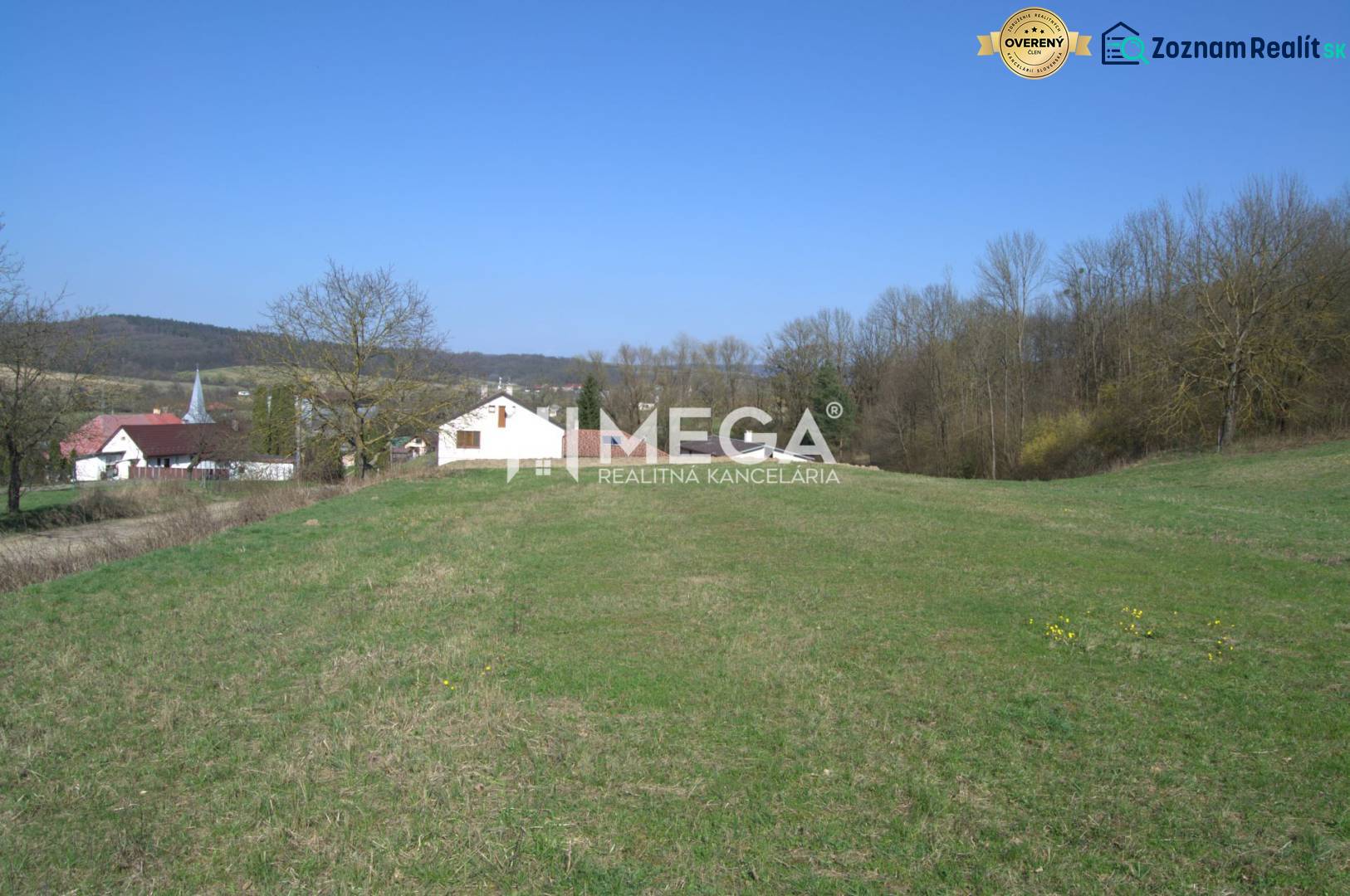 ZNÍŽENIE CENY-PREDAJ VEĽKÉHO POZEMKU (7.048 m2) v  obci Tovarnianska P - Pozemky - bývanie v Tovarnianskej Polianke, s výhľadom na domy a stromy pod modrou oblohou.