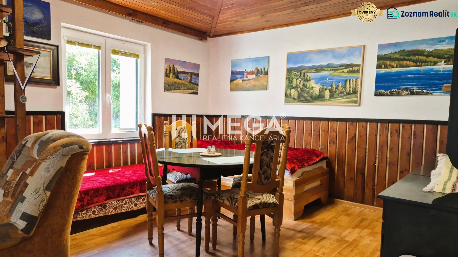 PREDAJ REKREAČNEJ CHATY NA DOMAŠI časť DOBRÁ - Izba na chate s dreveným stropom a podlahou s dreveným dekorom, obrazy na stenách.