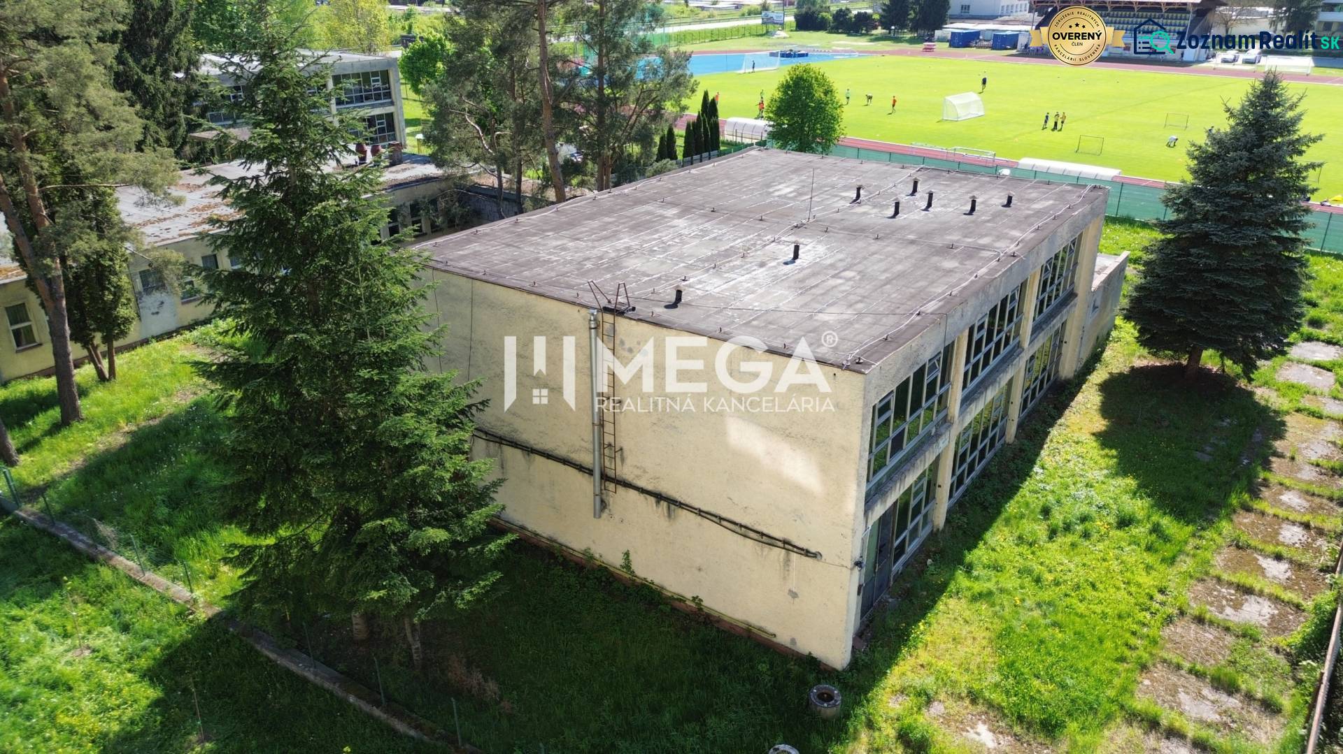 EXKLUZÍVNE NA PREDAJ budova na sídlisku 2A v meste Humenné - Budova na Tyršovej ulici v Humennom, obklopená stromami a športovým ihriskom v pozadí.