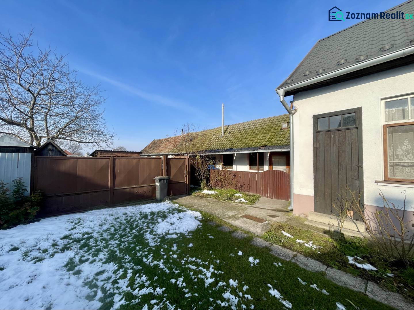 VRAKÚŇ –VEĽKÝ STAVEBNÝ POZEMOK (24 ÁROV) SO STARÝM RODINNÝM DOMOM NA P - Rodinný dom vo Vrakúni s dvorom, bránou, stromom a čiastočne zasneženým trávnikom.