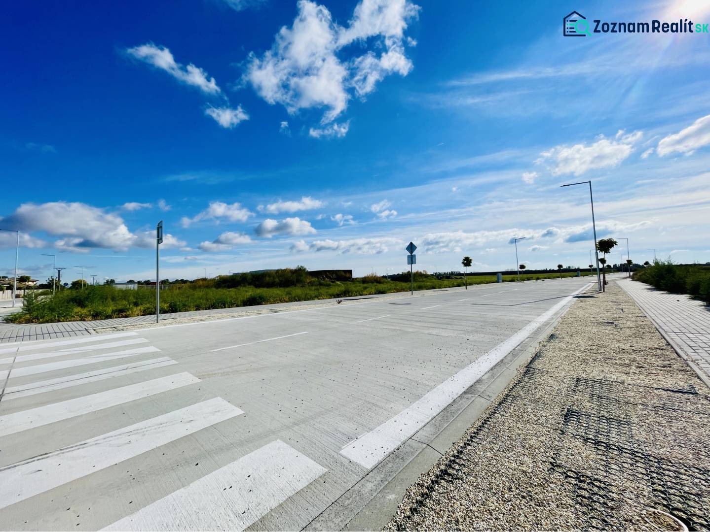 DUNAJSKÁ STREDA – SLNEČNÉ STAVEBNÉ POZEMKY NA PREDAJ V PROJEKTE VINICA - Cesta a chodník v Dunajskej Strede, pozemky - bývanie, neuvedená ulica pod modrou oblohou.