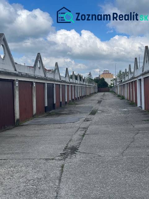 Garáž na prenájom v centre mesta. - Radu garáží tvorí ulica pod modrou oblohou s oblakmi.