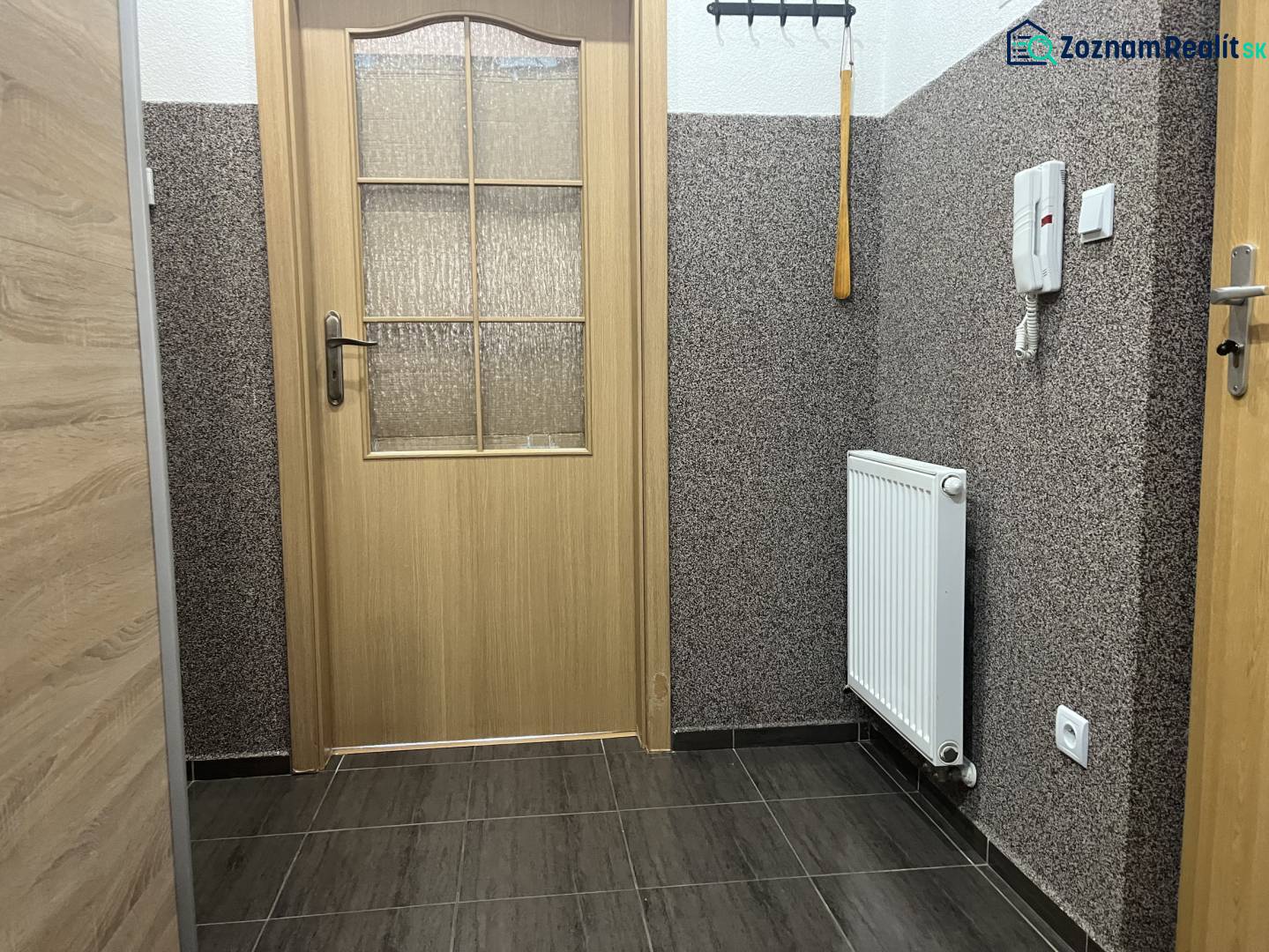 Štartovací 2-izbový byt s balkónom a klimatizáciou – Ohrady - Interiér 2-izbového bytu s dlažbou, radiátorom, dverami so sklom a svetlými stenami.