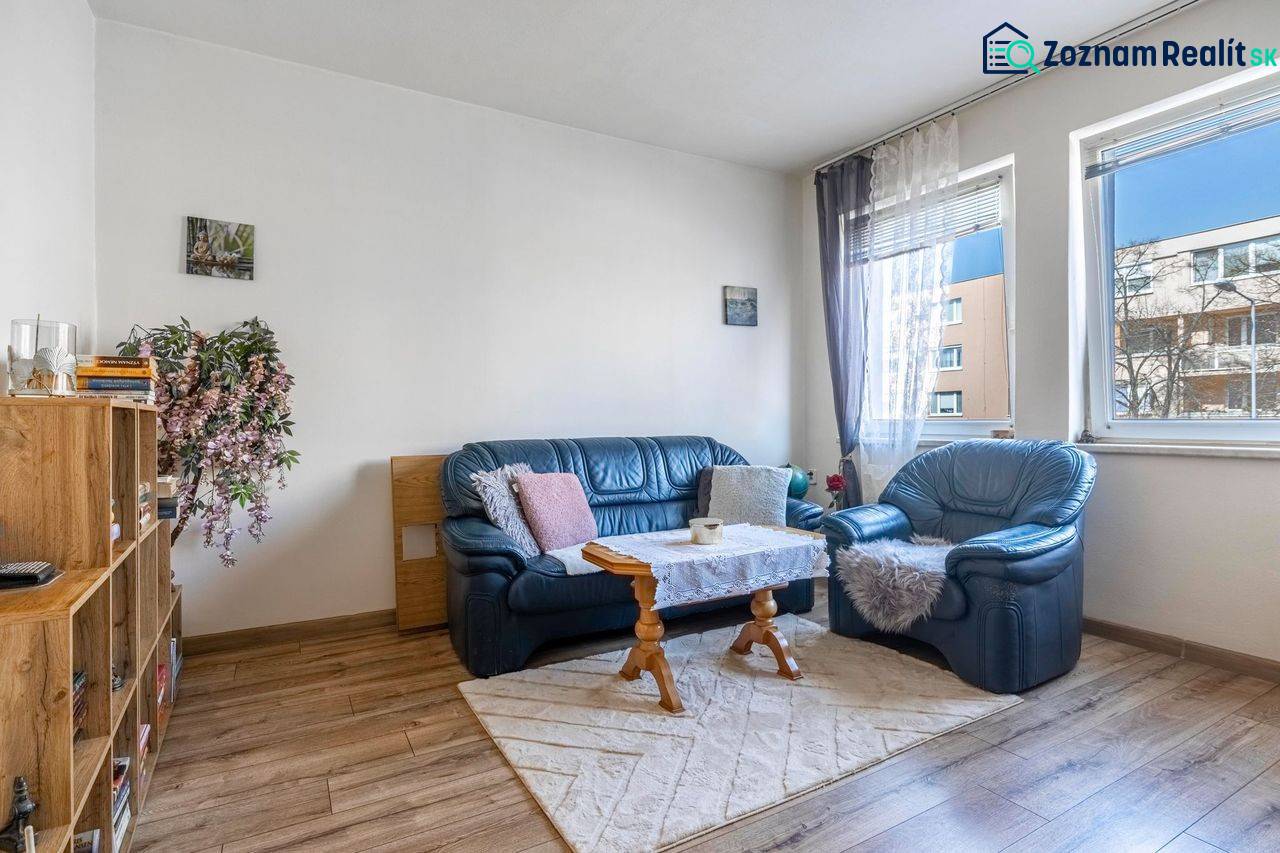 ☎️ 0918197701- PREDAJ - Nebytových priestorov Dunajská Streda - Pohodlný obývací priestor, modré kreslá, koberec, knihovnička, podlaha s dreveným dekorom.