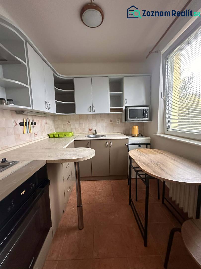 REZERVOVANÉ  ☎️ 0918/197 701 Na prenájom garsónka blízkosti centra mes - Kuchyňa v rekreačnom apartmáne s bielymi skrinkami, barovým pultom a mikrovlnkou.