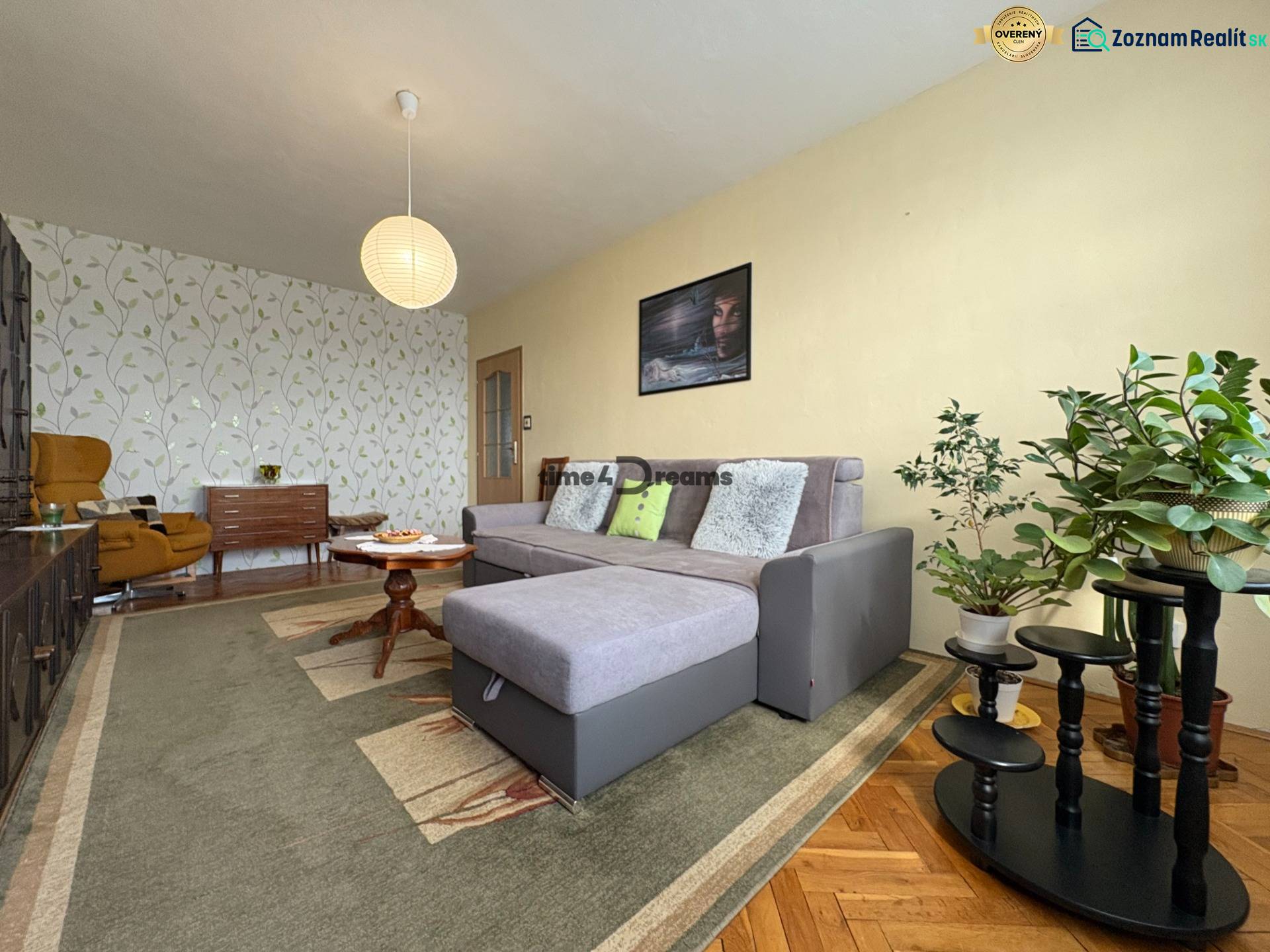 Na predaj: CENTRUM veľký 3 izb.byt + BALKON + ŠATNIK - Opis obývacej izby, sivý gauč, rastliny, vzorovaná tapeta, koberce, atmosféra a 3-izbový byt.