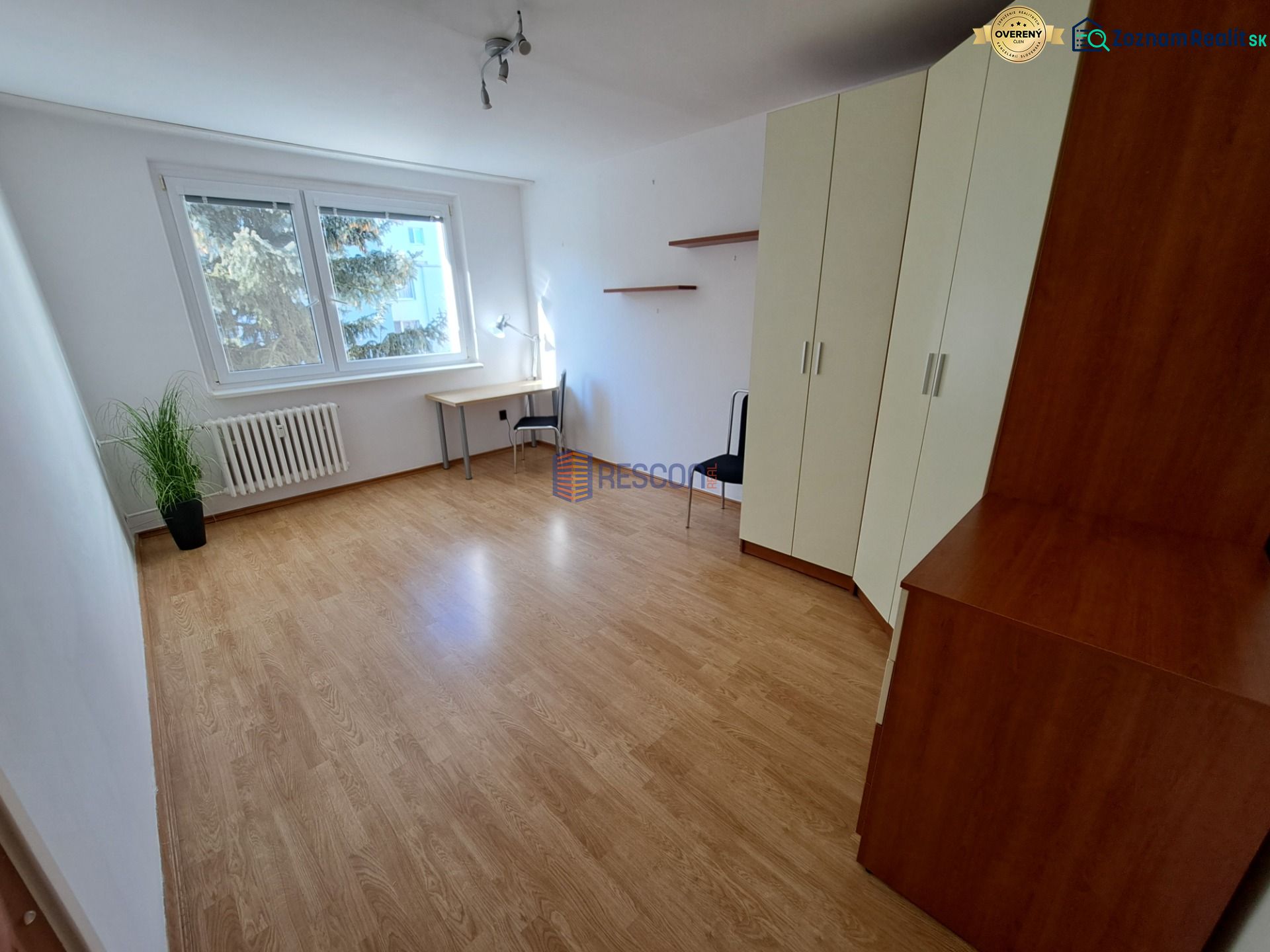 2-izbový byt, 51 m², samostatné izby, tichý, výhľad do zelene,K.Adlera - Izba s podlahou s dreveným dekorom, veľkými oknami, skriňou a písacím stolom.