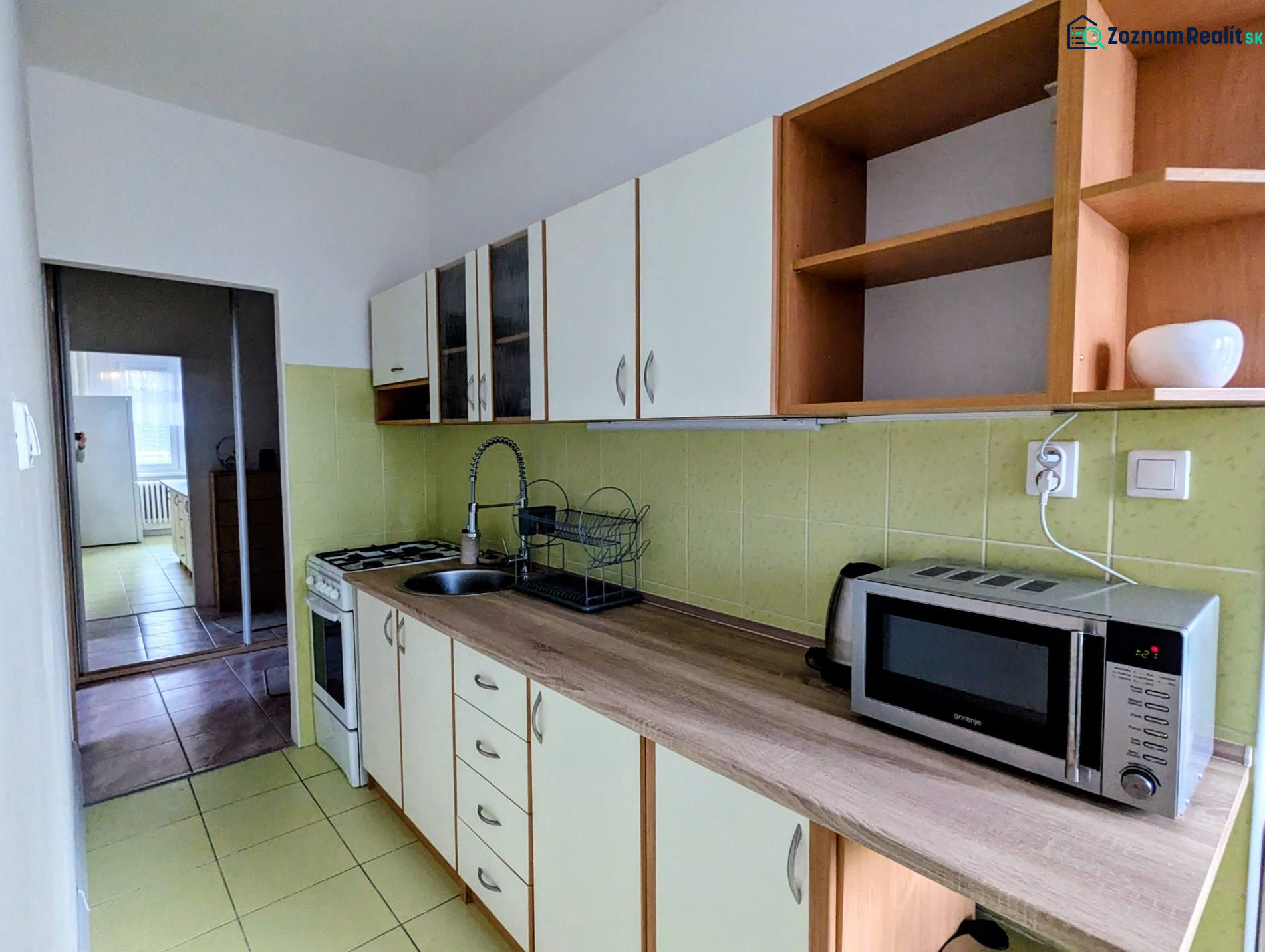 2izbový byt na prenájom v Dubnici nad Váhom  - Kuchyňa v 2-izbovom byte s mikrovlnkou a varnou doskou, smerujúca do ďalšej miestnosti.