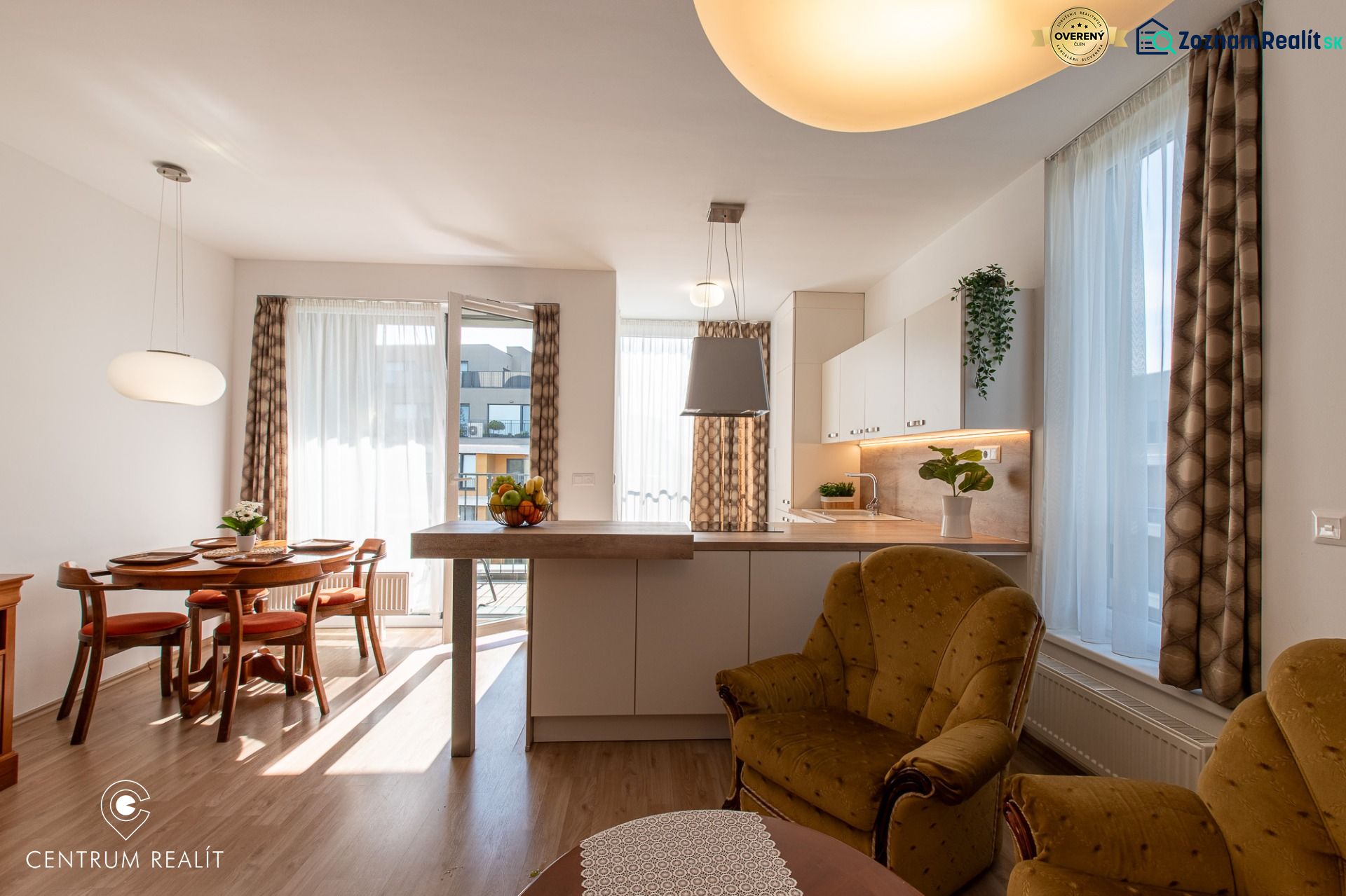 Moderný 2-izbový apartmán s parkovaním, Vila Leonardo, Bajkalská - Obývačka spojená s kuchyňou, jedálenský stôl, podlaha s dreveným dekorom, svetlé závesy.