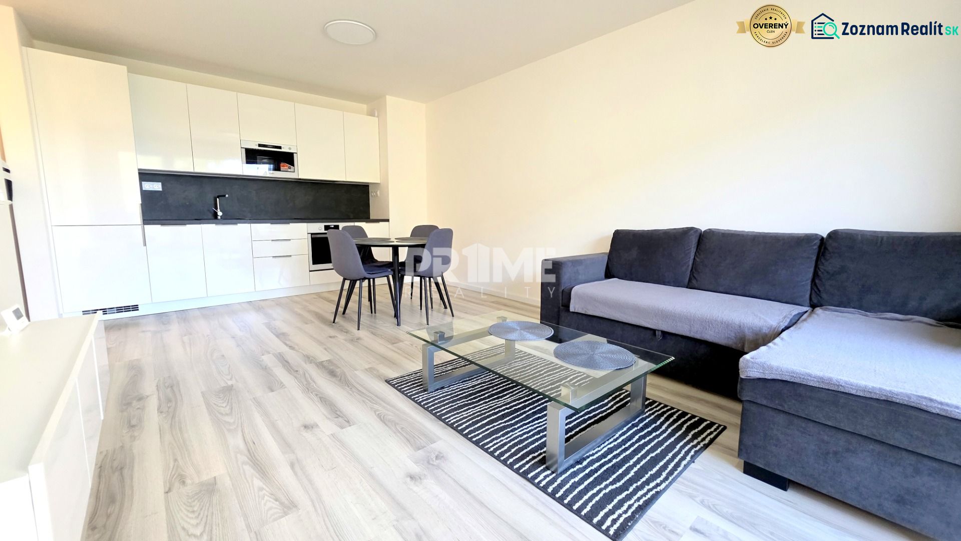 MODERNÝ 2i byt, POD VINICOU, LOGGIA, PARKING, Nové Mesto - Obývacia izba v 2-izbovom byte s podlahou s dreveným dekorom a kuchynskou linkou.