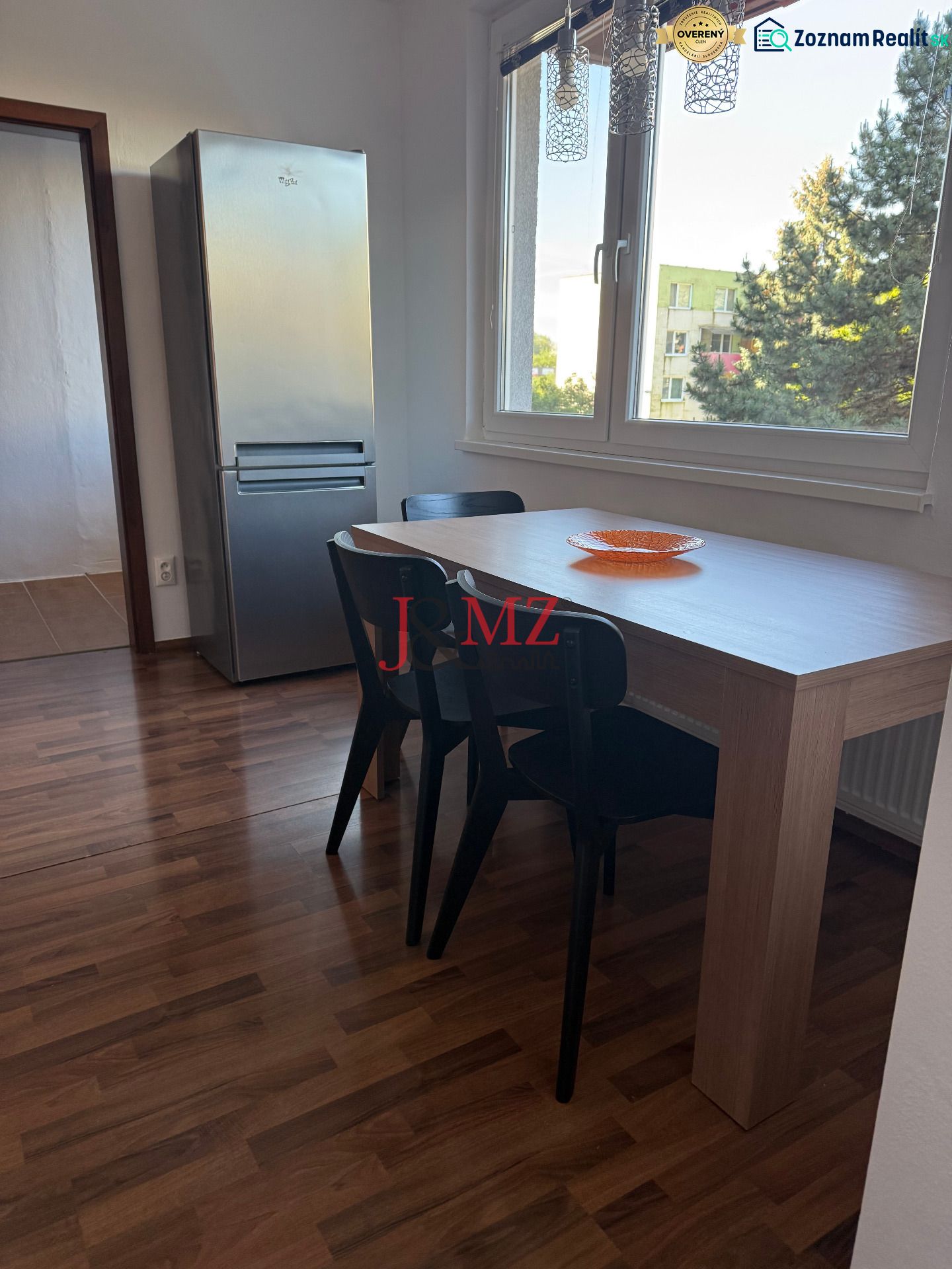 Prenájom 3-izb. byt Ku Bratke - zariadený - Jedálenský kút s tromi stoličkami a stolom, vedľa chladničky, podlaha s dreveným dekorom.