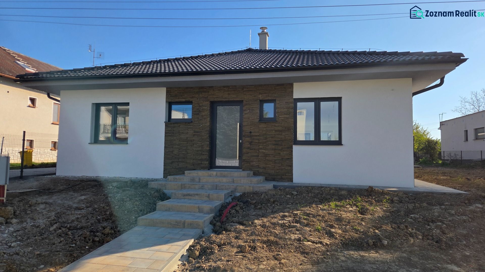Bungalov v centre obce Cabaj Čápor, Wágnerova ulica, Dom č.1 - Rodinný dom v Cabaji-Čápore s bielou fasádou a kamenným obložením, svahovitý terén.